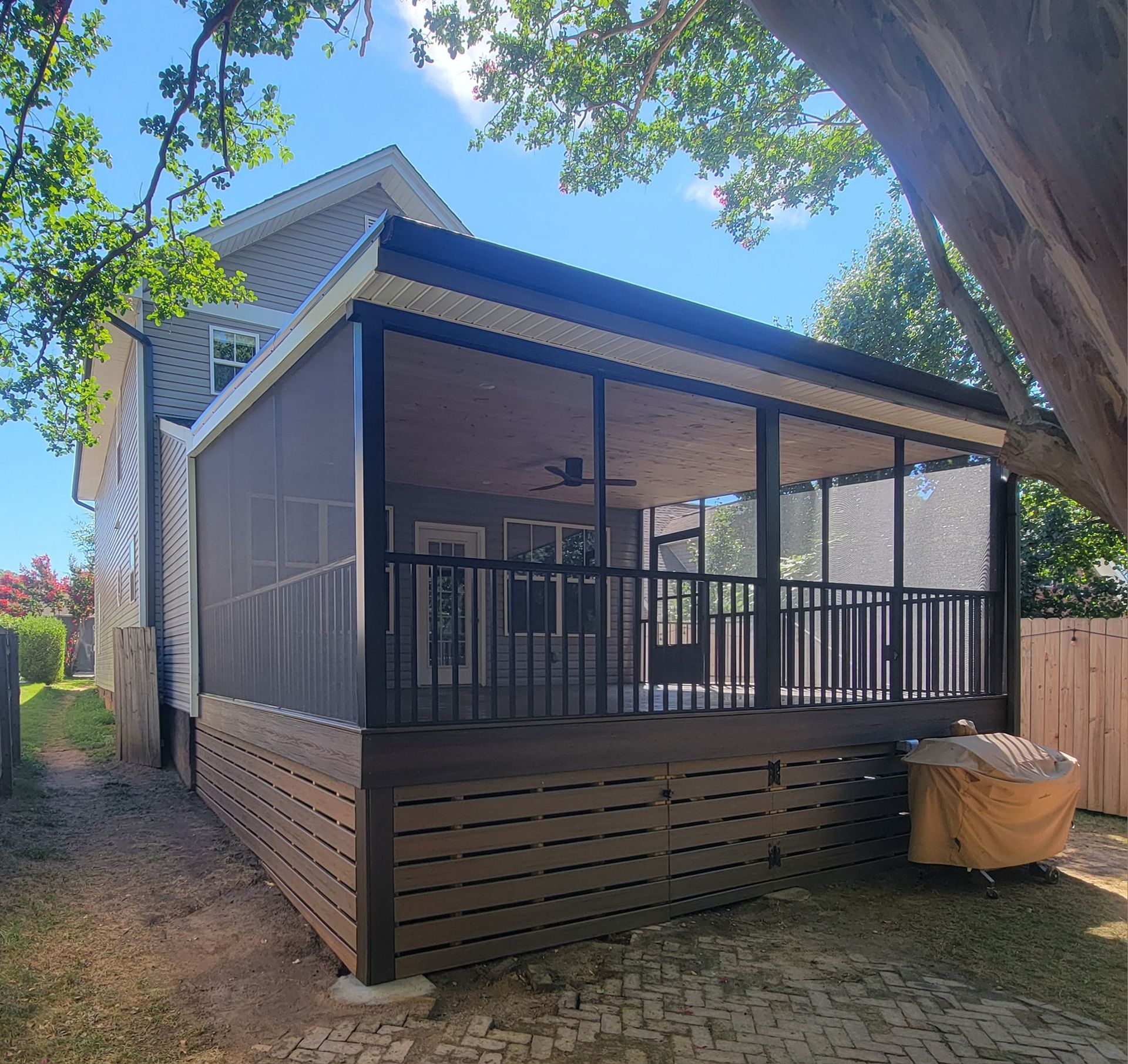 Screened-in deck attached to a two-story house with dark brown composite decking and railing.