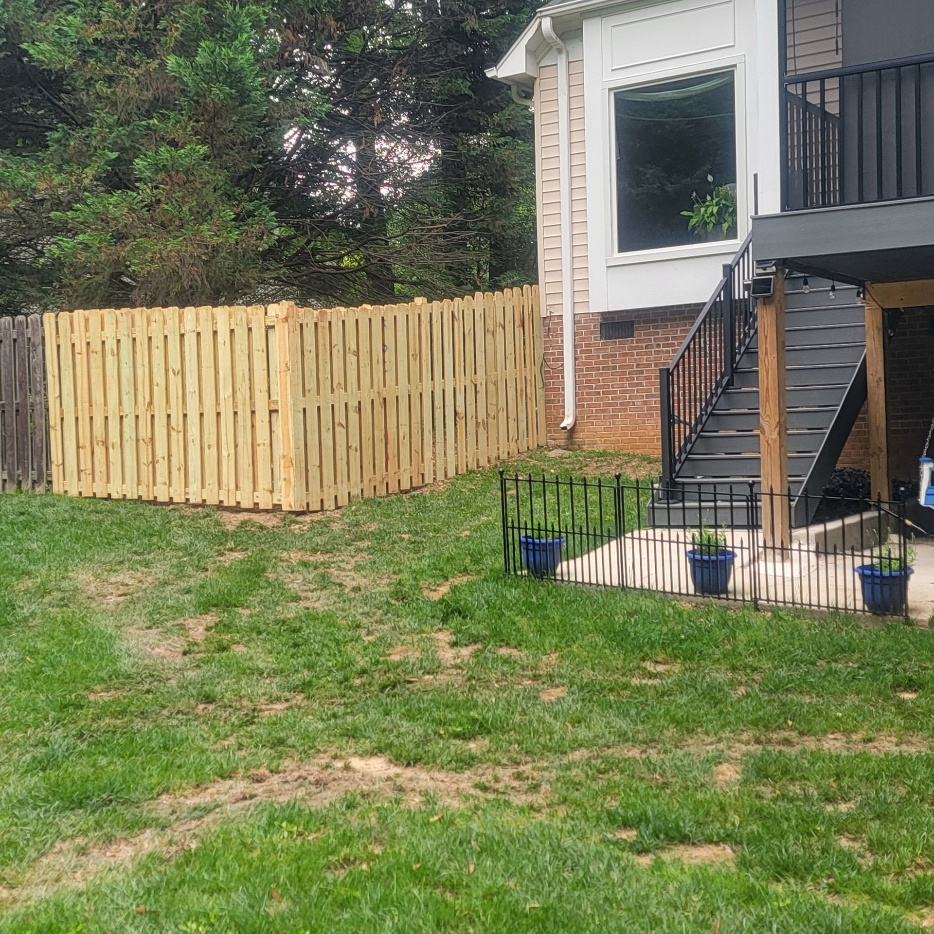 Wooden fence surrounding a backyard with a house, stairs, and small decorative fence.