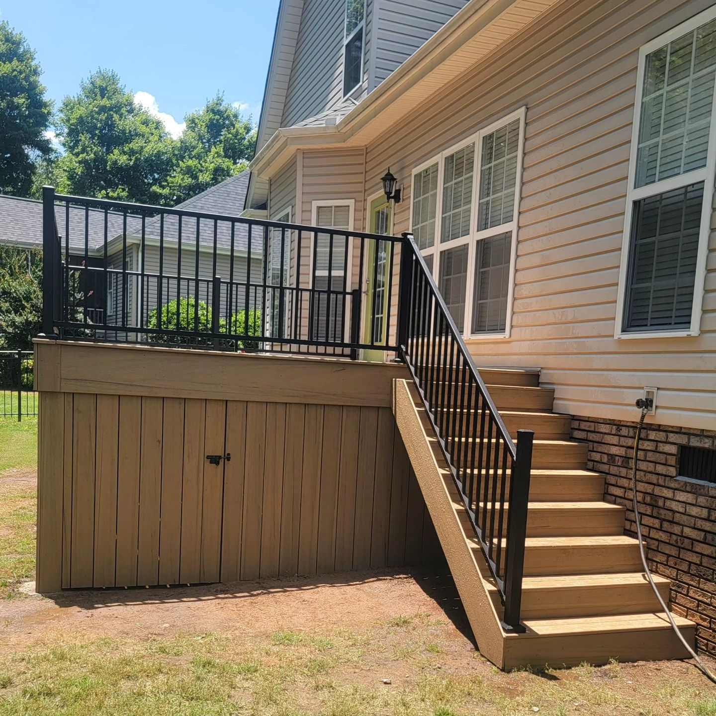 Deck with black railing and steps attached to a tan house.