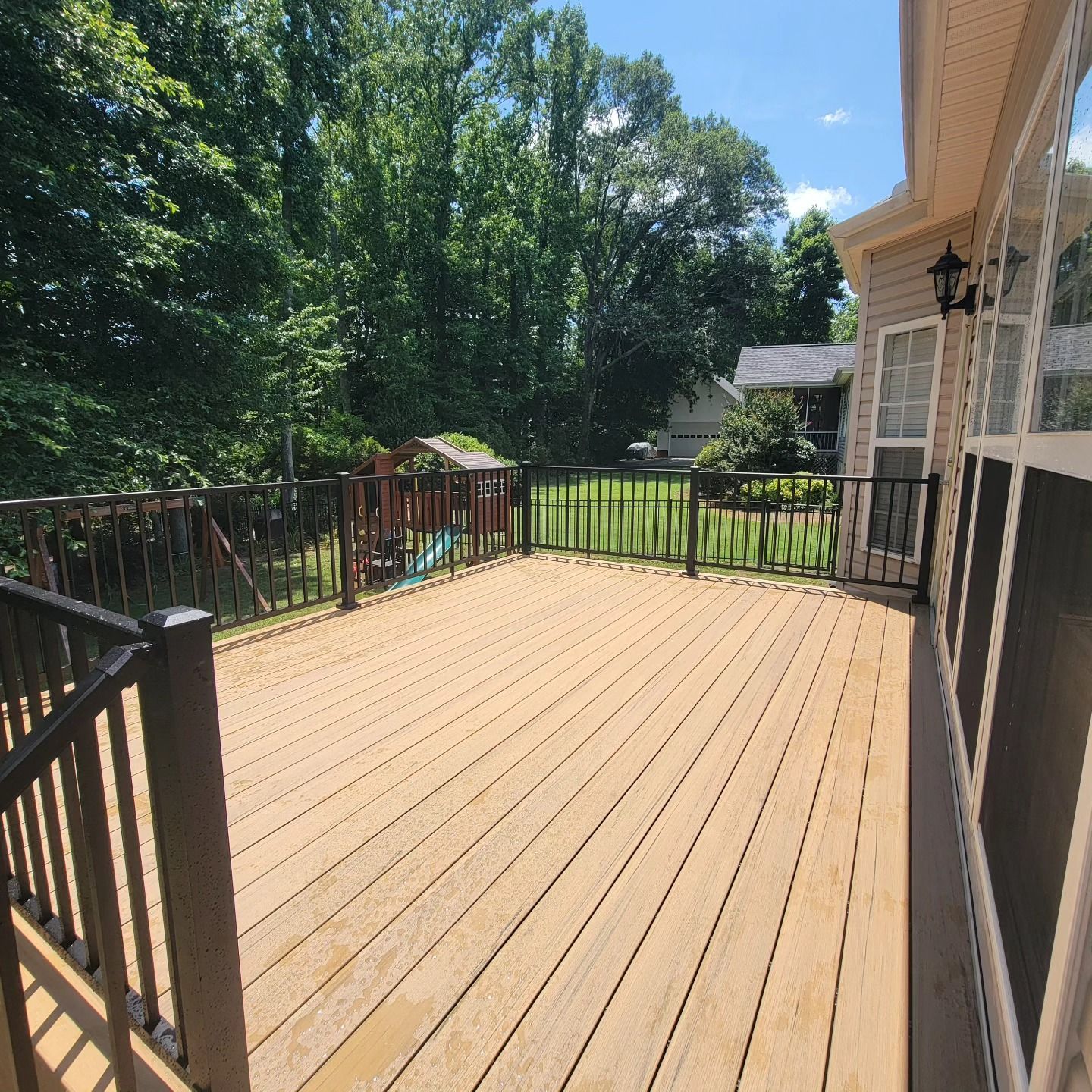 Wooden deck with black railings. A play set is in the yard, trees in the background. Sunny day.