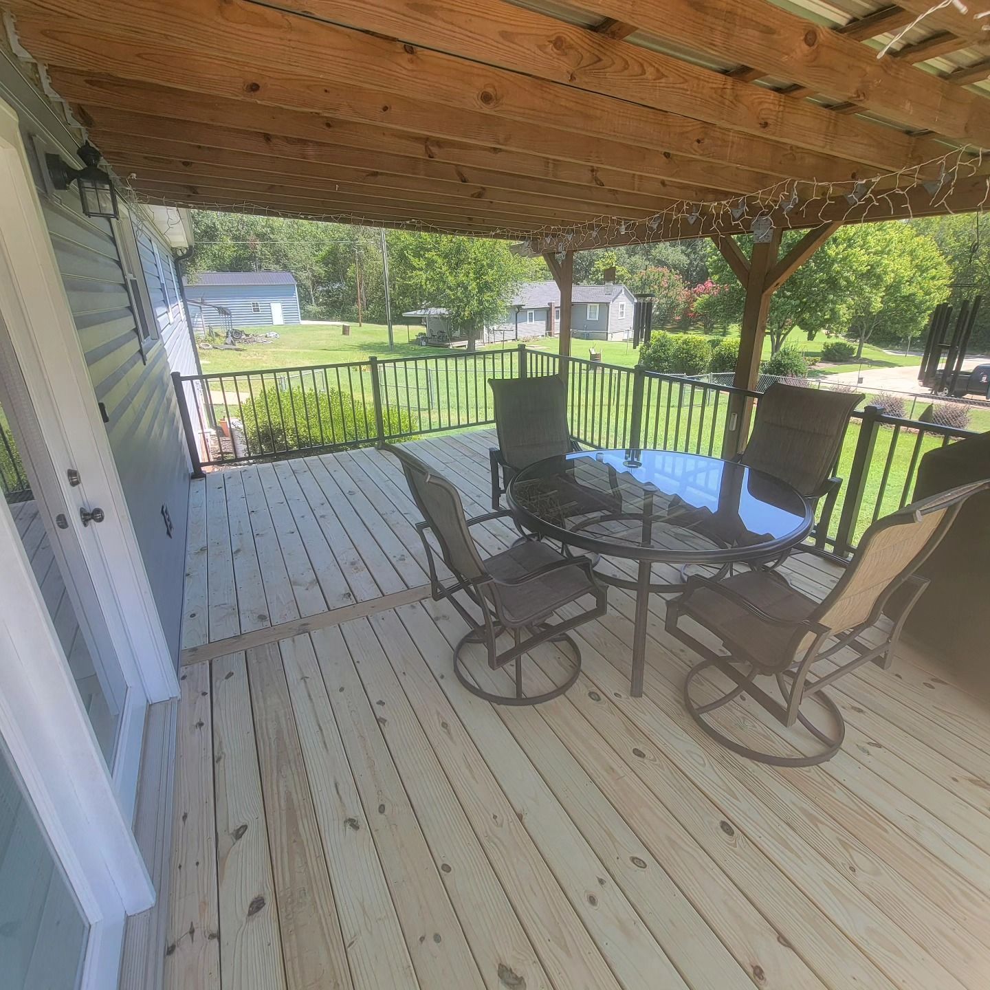 Wooden deck with outdoor furniture under a covered area. Green yard in background.