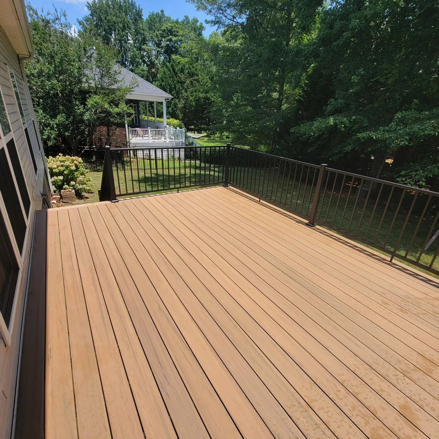 Wooden deck with black railing overlooking a yard with a gazebo and trees.