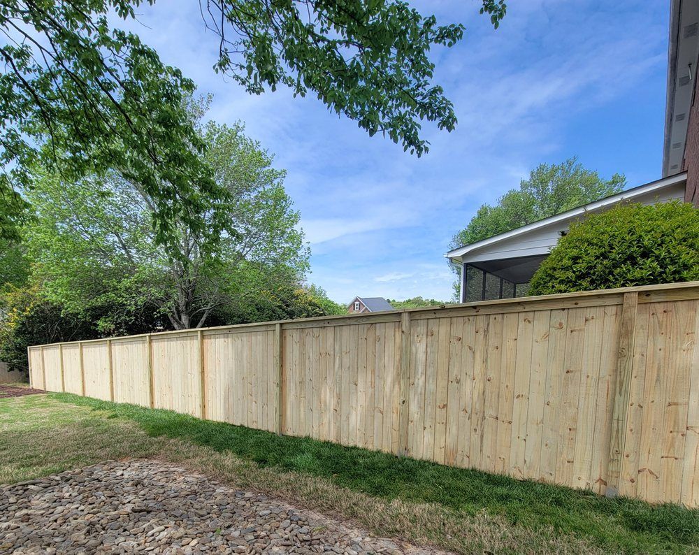 Wooden fence along green grass, under a blue sky with trees.