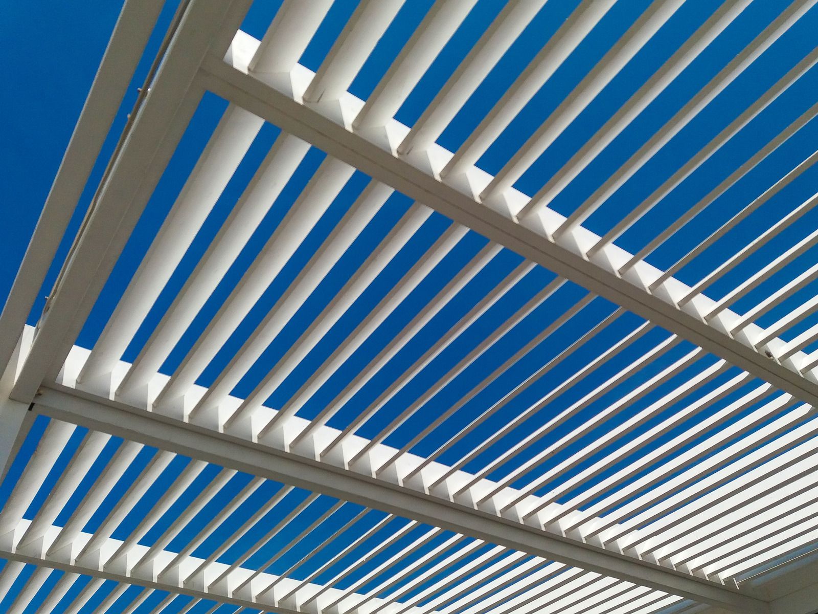 White slatted pergola against a bright blue sky.