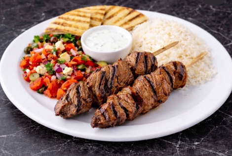 Grilled meat skewers with rice, salad, pita bread, and tzatziki sauce.