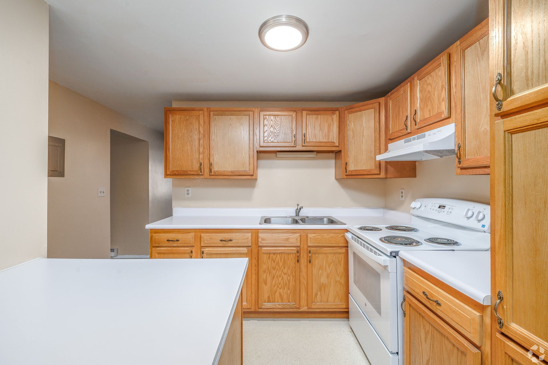 Empty kitchen with light wood cabinets, white appliances, and a white island countertop.