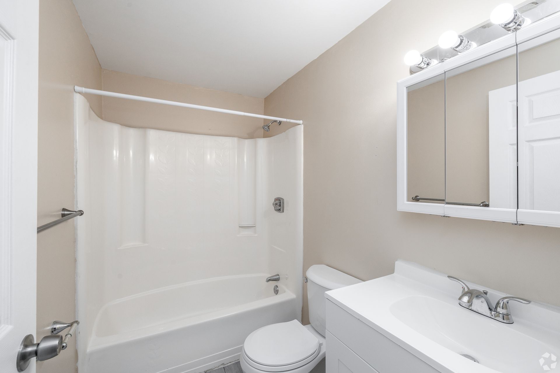 Bright bathroom with white tub, shower curtain, toilet, and vanity with mirror lights.