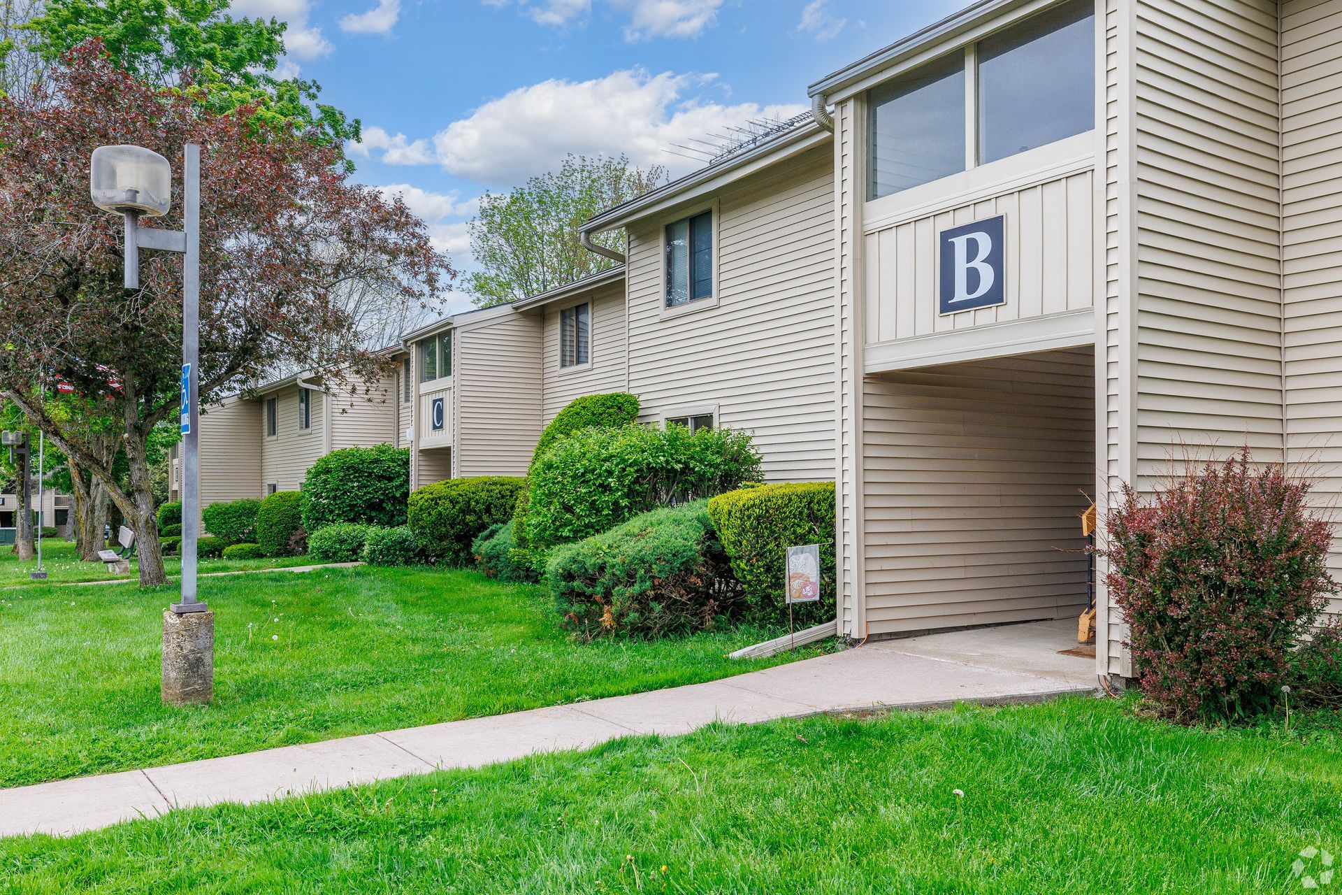 Apartment building entrance with a blue B sign, sidewalk, and green lawn on a cloudy day