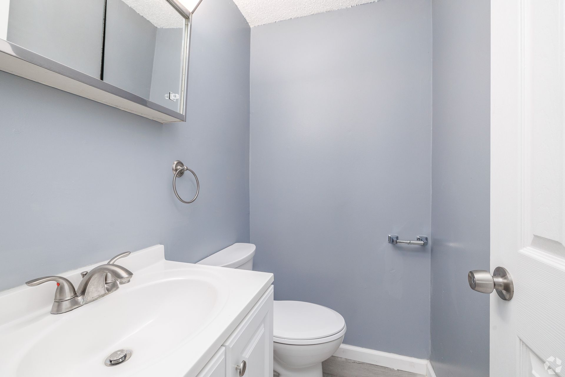 Small bathroom with white vanity, toilet, light gray walls, and an open door.