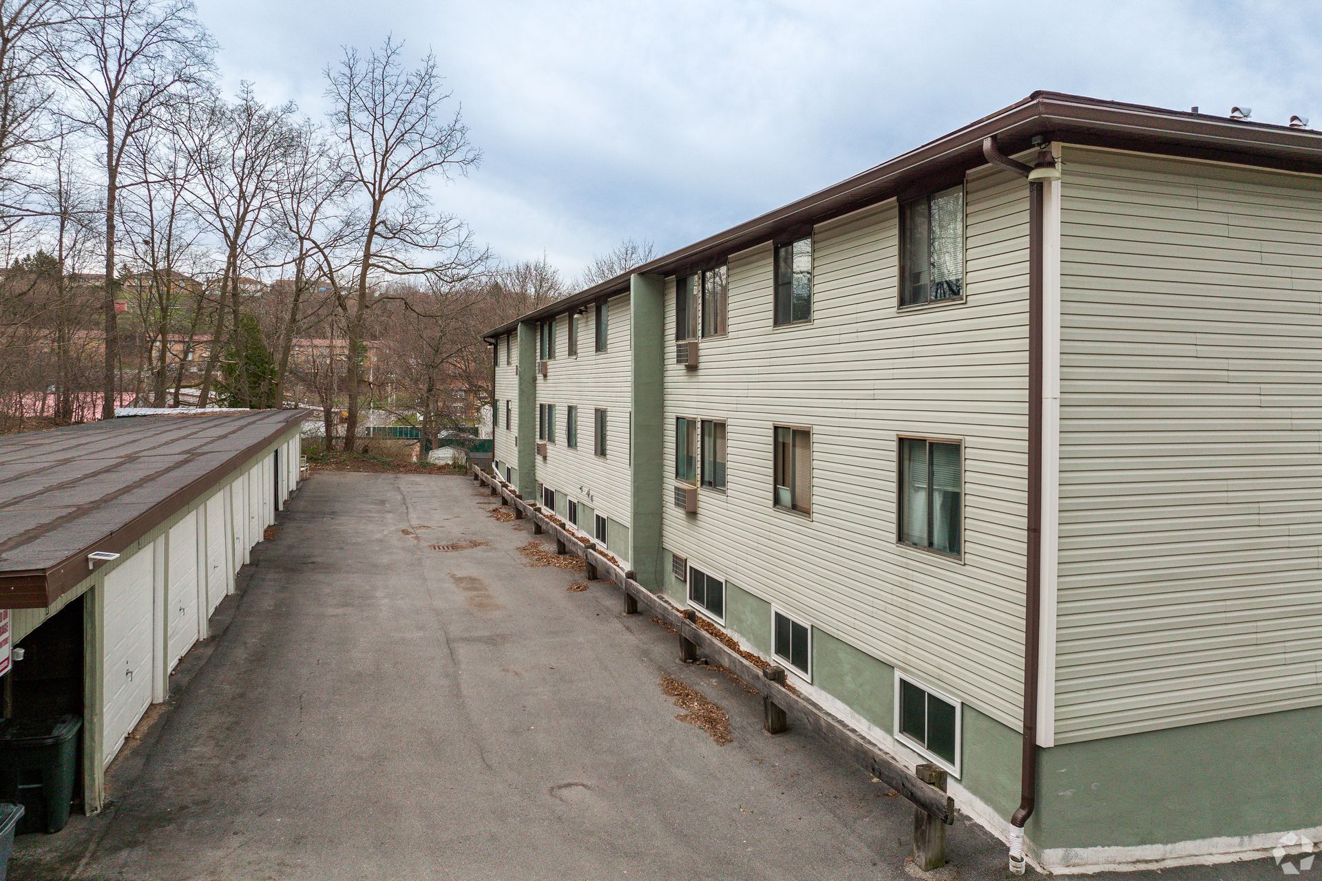 Exterior of a motel-style apartment building with parking lot and trees on a cloudy day