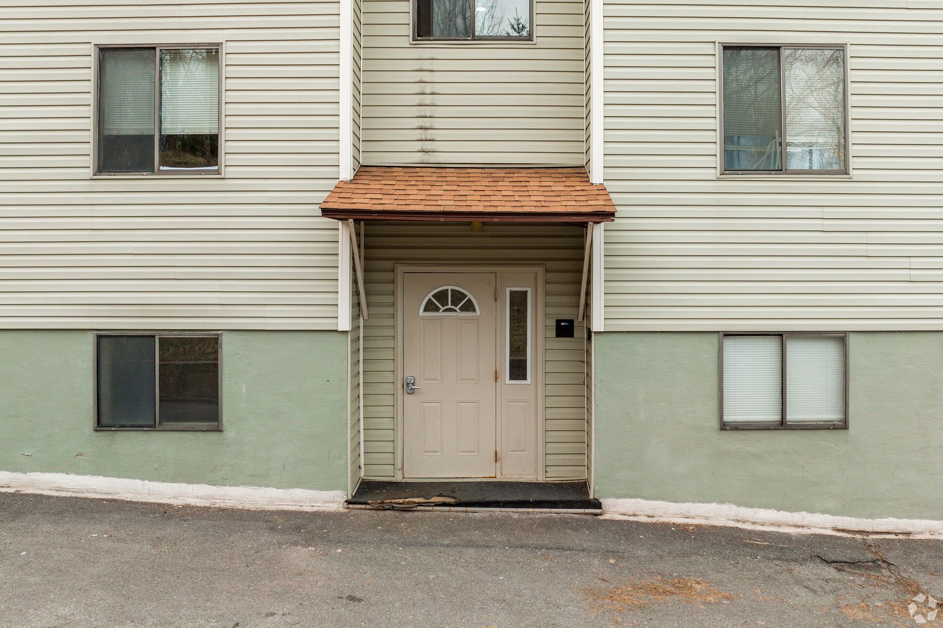 Apartment building entrance with beige door, green lower siding, and small copper awning