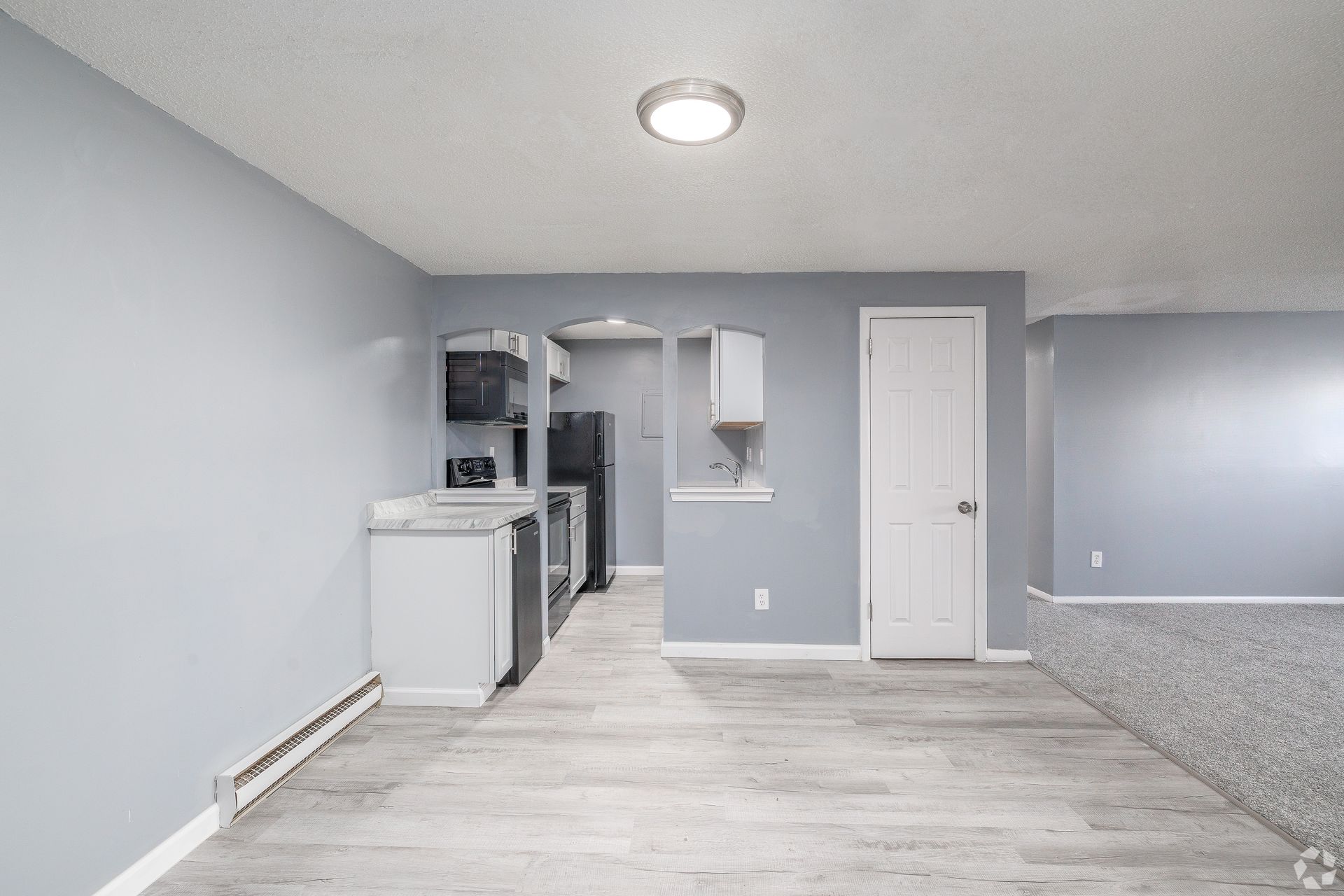 Empty gray basement room with white appliances, light wood floor, and a closed white door