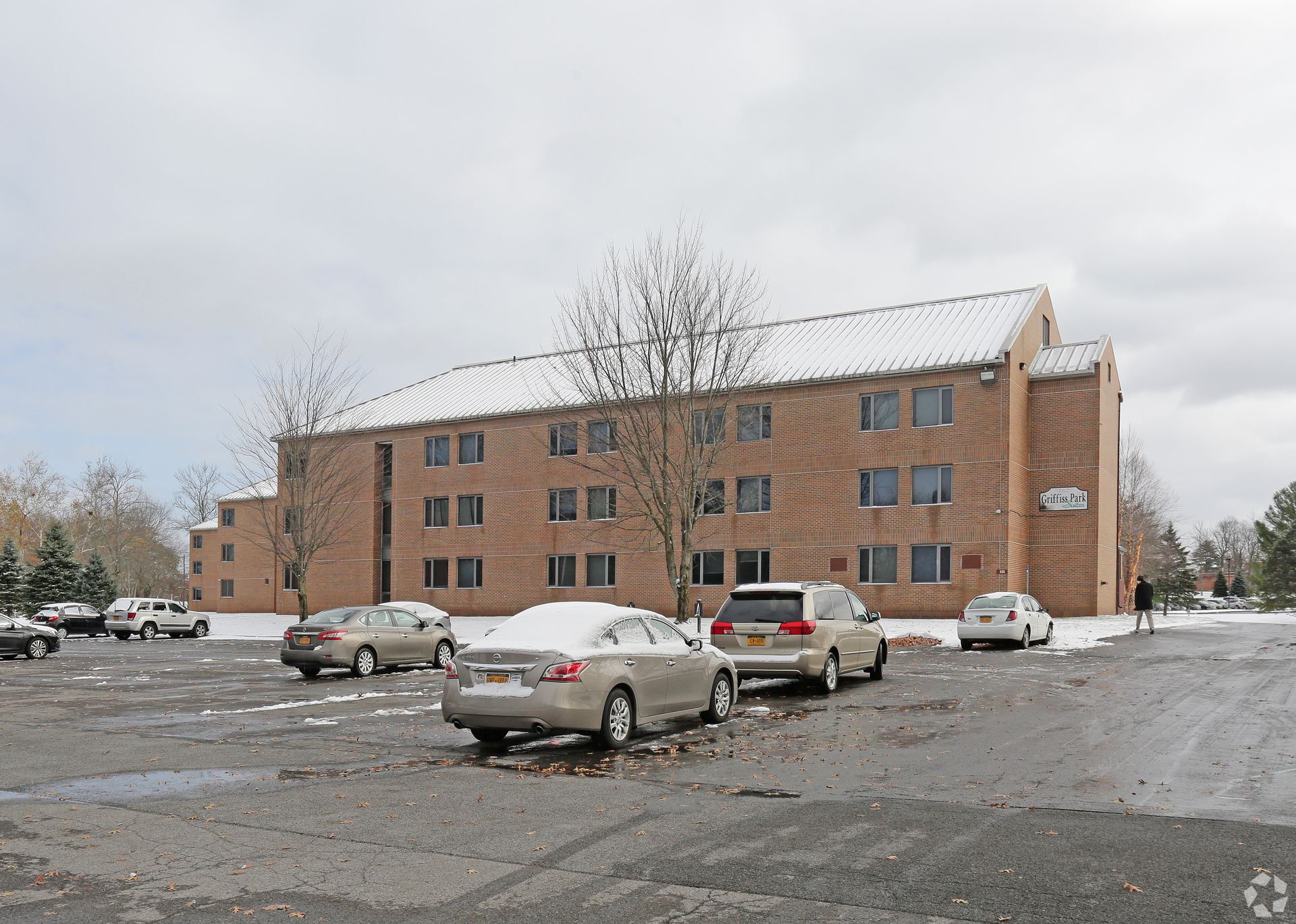 Brick building with parked cars in a snowy parking lot under an overcast sky