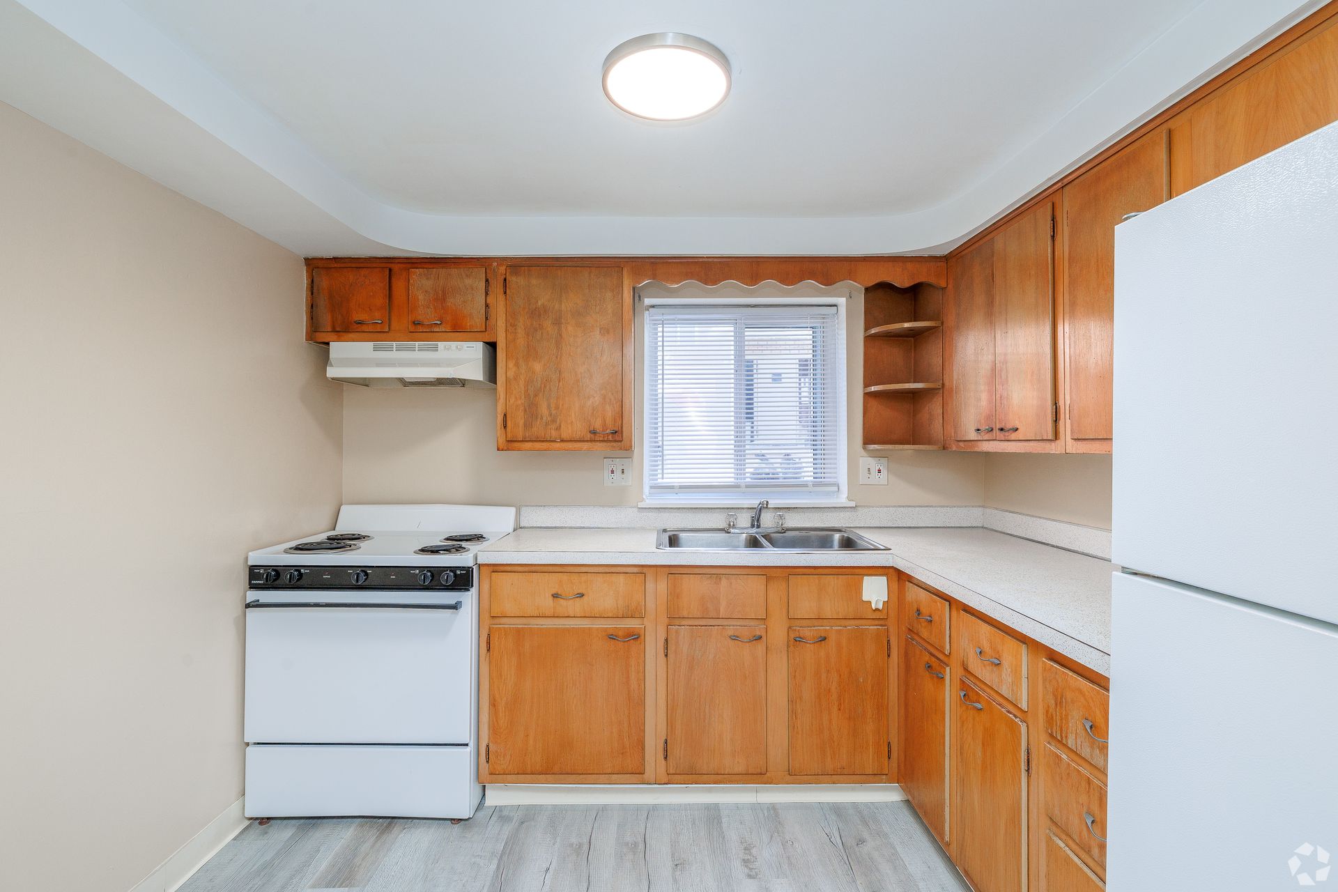 Small kitchen with white appliances, wood cabinets, and a window over the sink.