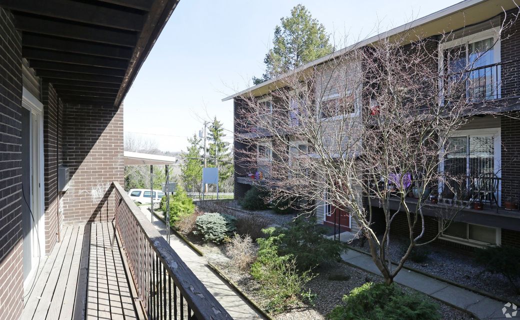 Apartment courtyard with blossoming trees, brick buildings, and a walkway beside a balcony railing