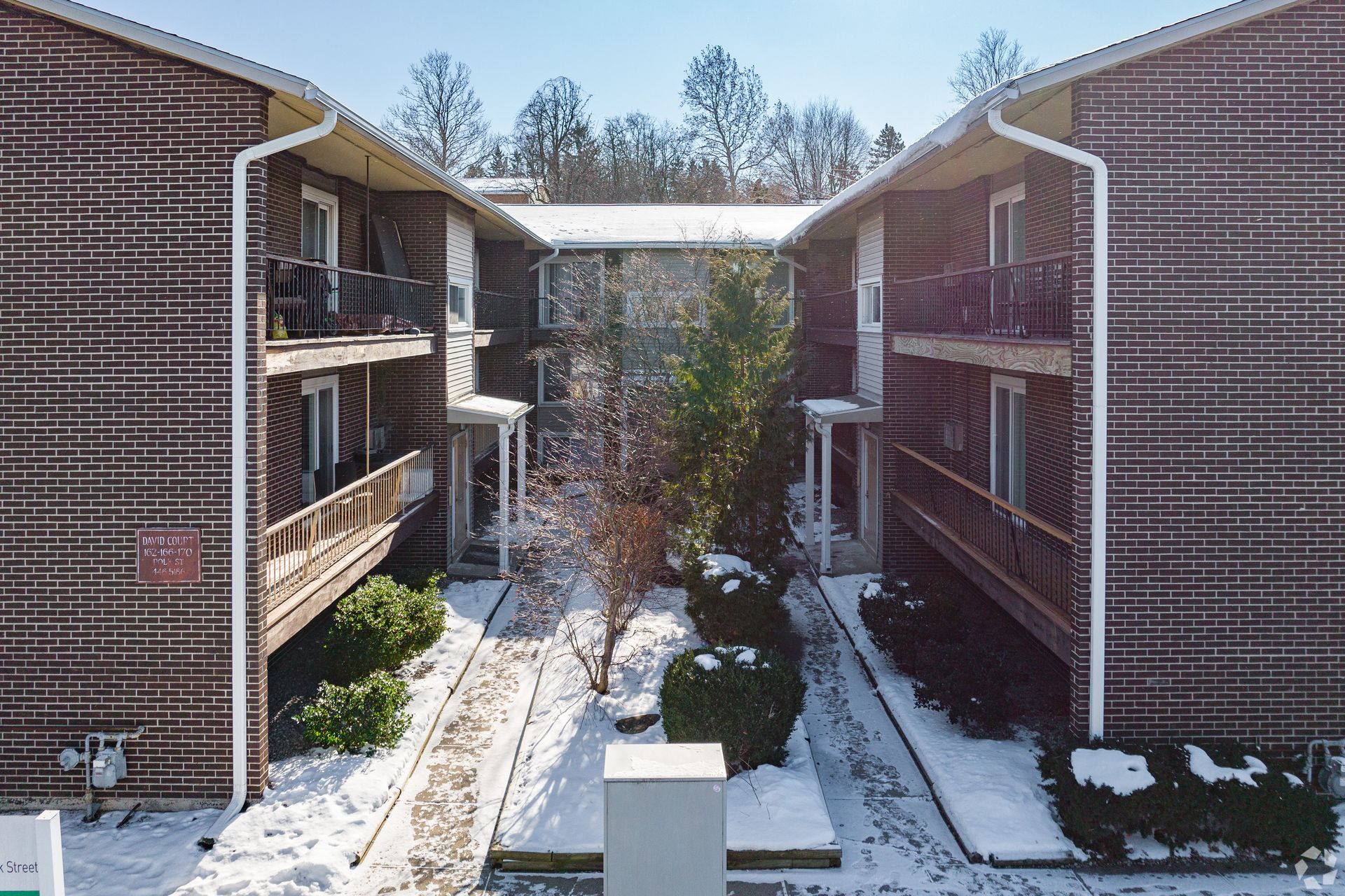 Snowy apartment courtyard between two brick buildings with balconies and trees