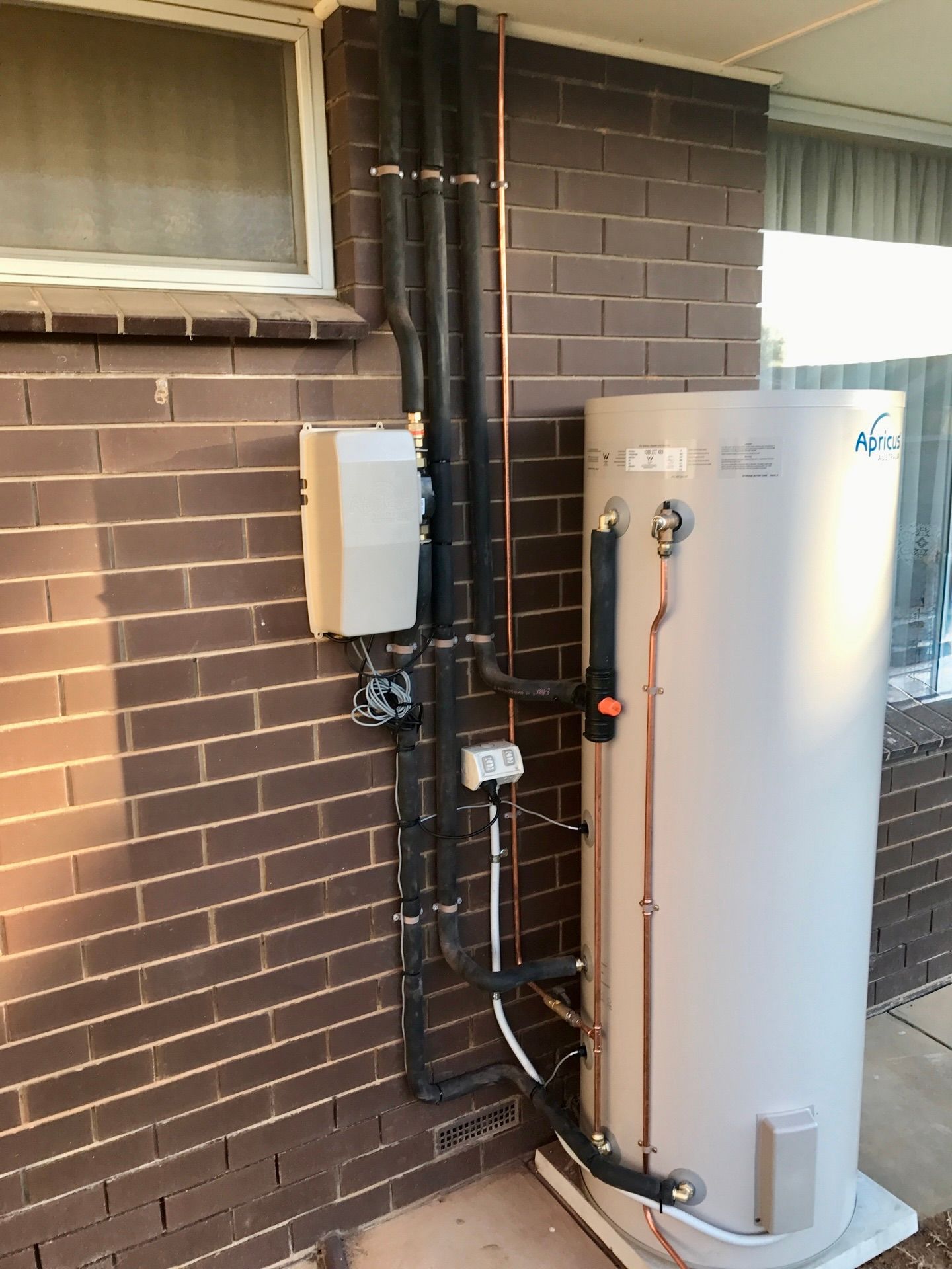 a white hot water unit next to a brick house wall — Essential Roofing and Plumbing in Wagga Wagga, NSW