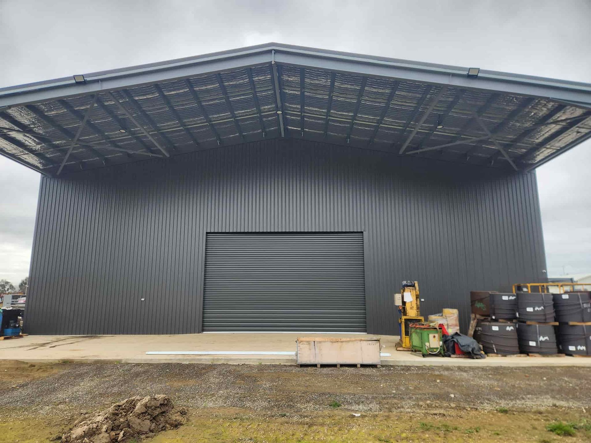 A Large Warehouse With a Large Garage Door is Being Built — Essential Roofing and Plumbing in Young, NSW