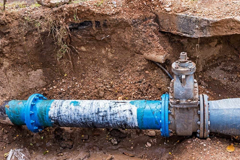 A Blue Pipe is Sitting in the Dirt Next to a Valve — Essential Roofing and Plumbing in Young, NSW