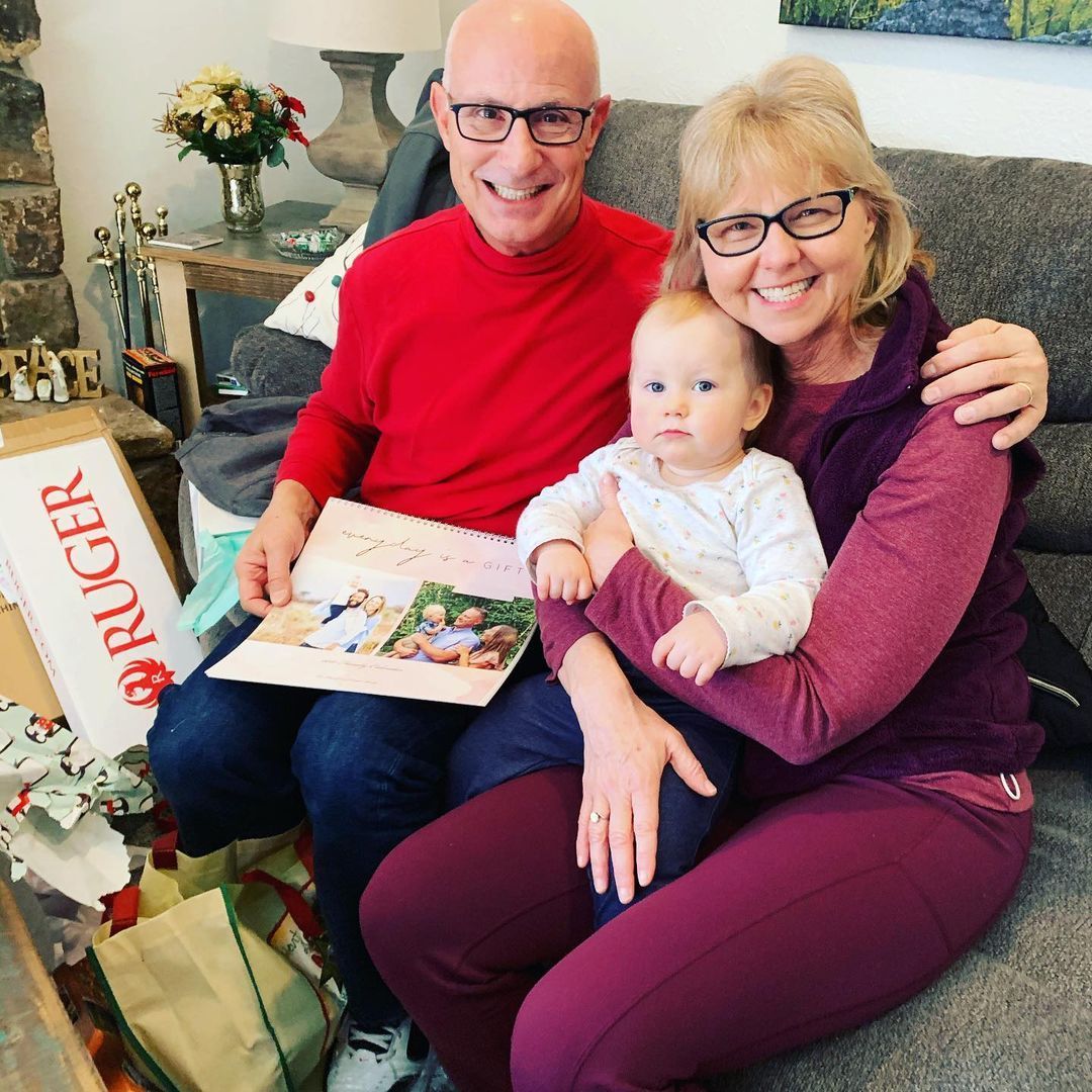 A man and woman are sitting on a couch with a baby and a box that says ruger on it