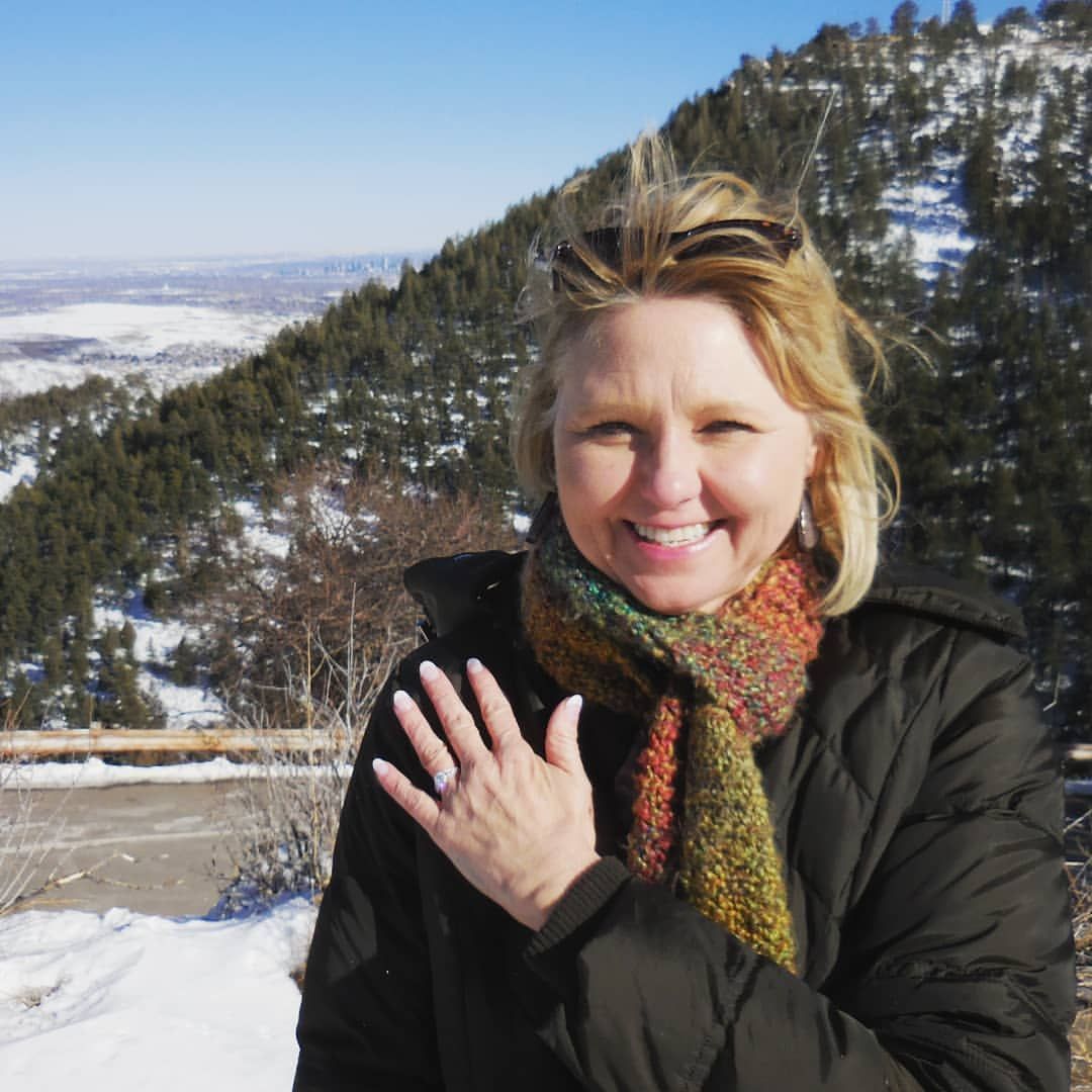 A woman wearing a scarf and sunglasses stands in front of a snowy mountain