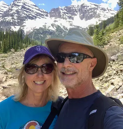 A man and a woman are posing for a picture in front of a mountain.