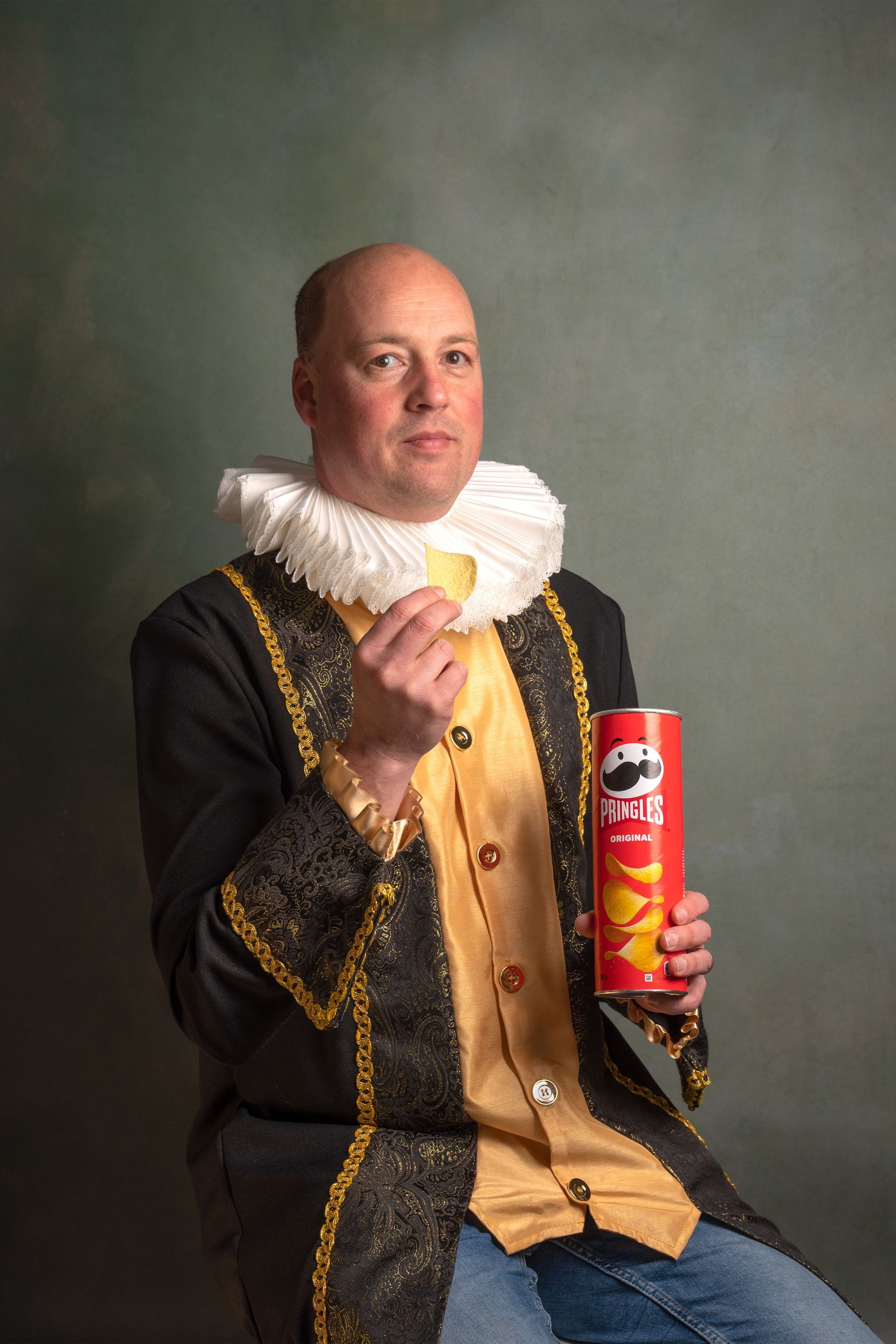 Een man in kostuum eet een aardappelchips en houdt een blikje pringles vast.