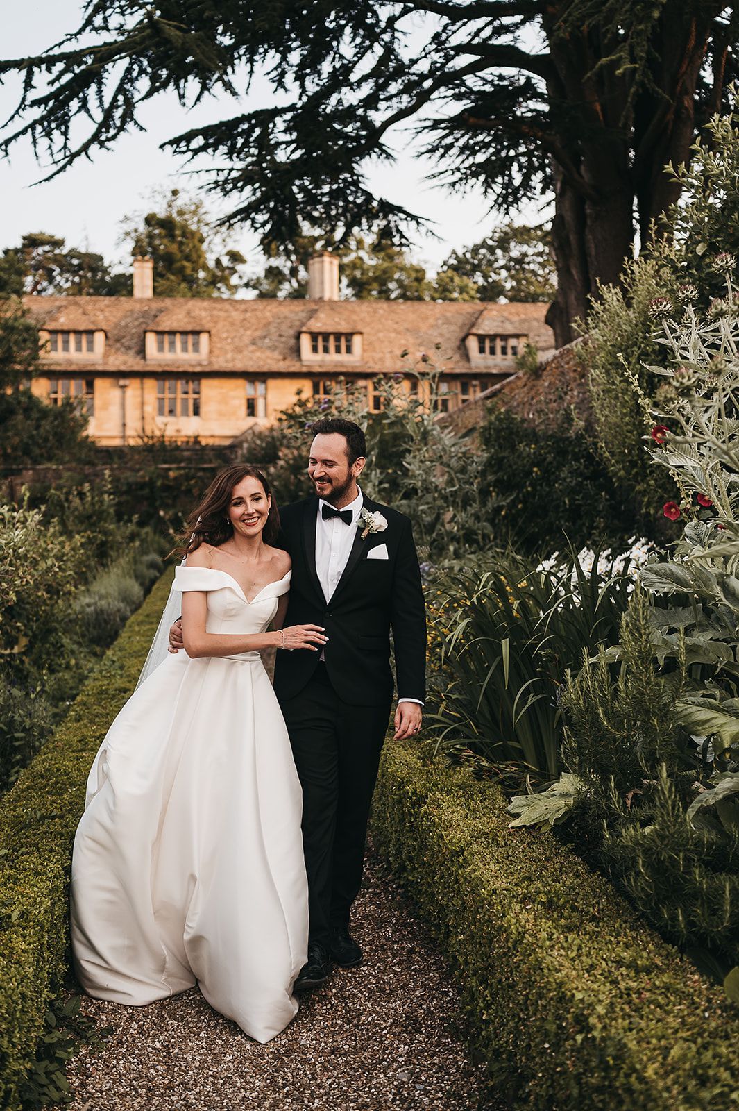 A bride and groom are walking down a path in a garden.