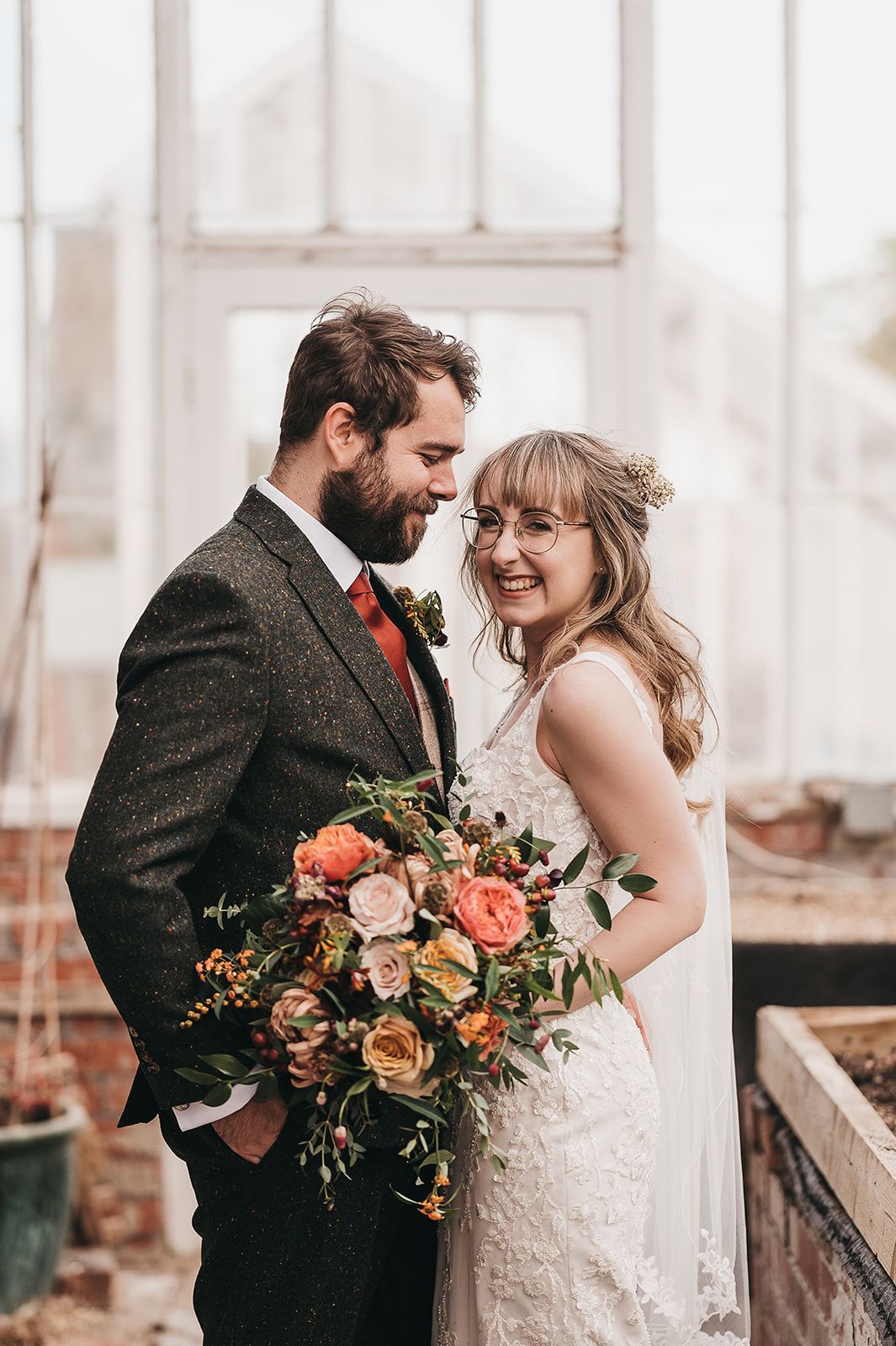 A bride and groom are posing for a picture in a greenhouse.