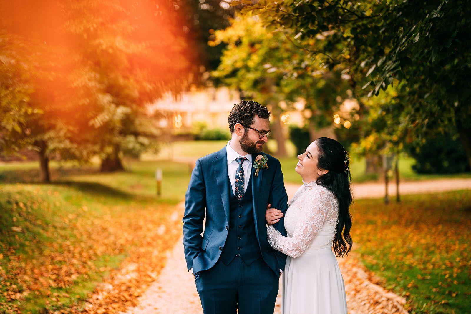 A bride and groom are standing next to each other on a path in a park.