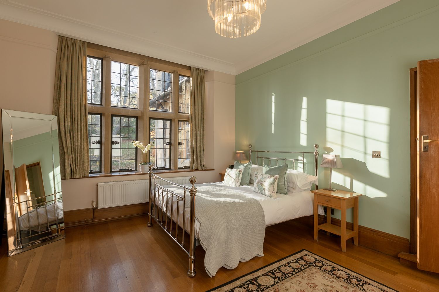 A bedroom with a bed , nightstand , mirror and window.