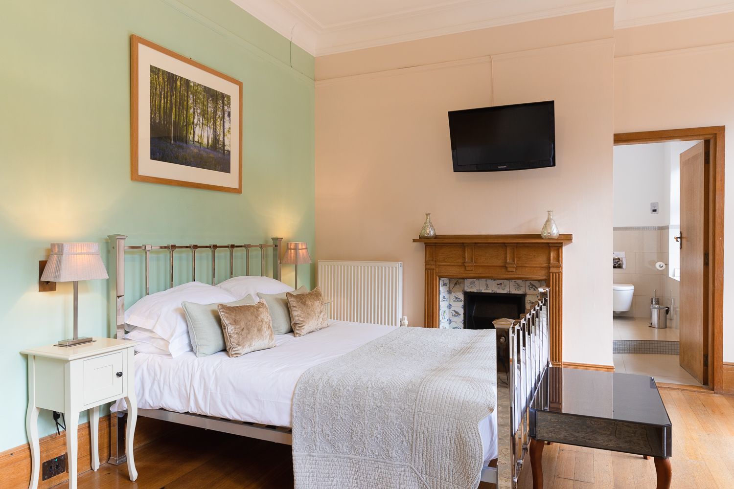 A bedroom with a bed , nightstand , television and fireplace.