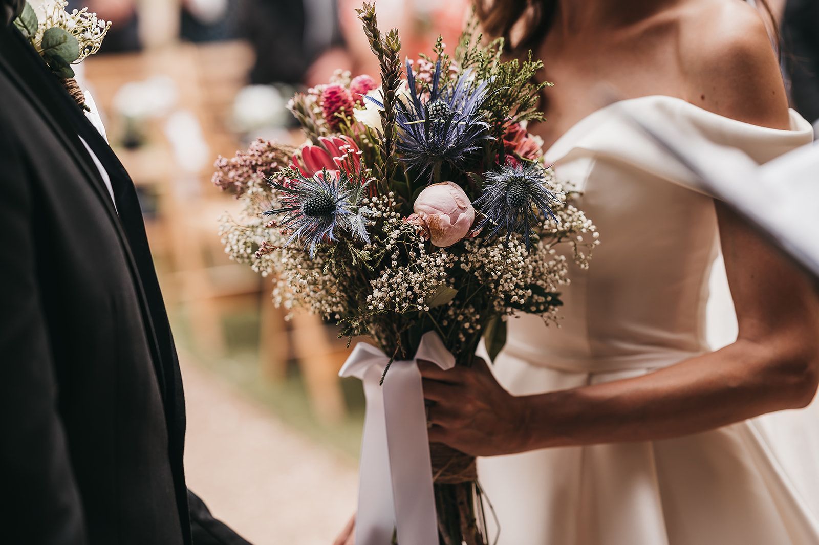 A bride and groom are holding hands and the bride is holding a bouquet of flowers.
