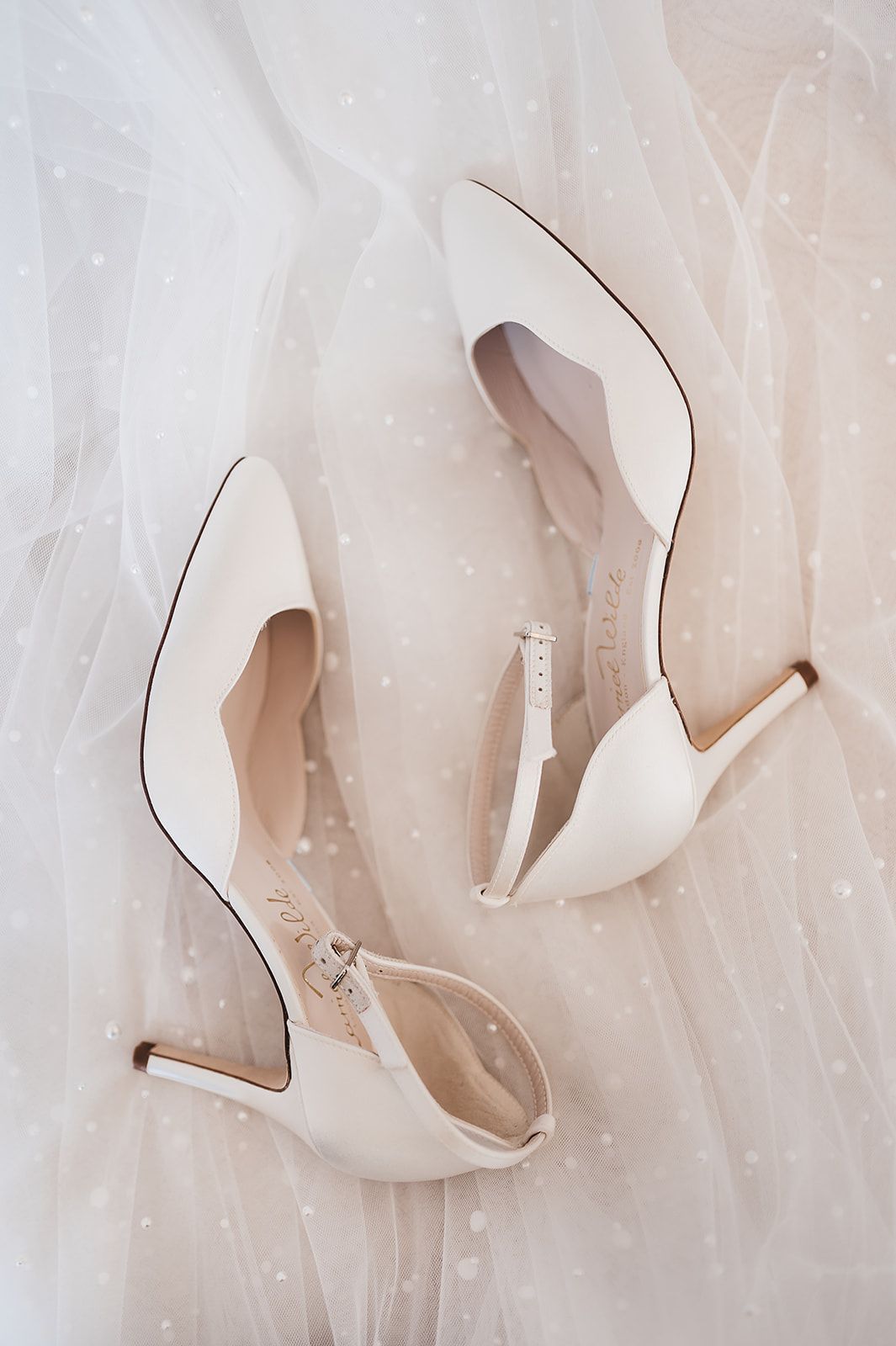 A pair of white wedding shoes are sitting on top of a white dress.