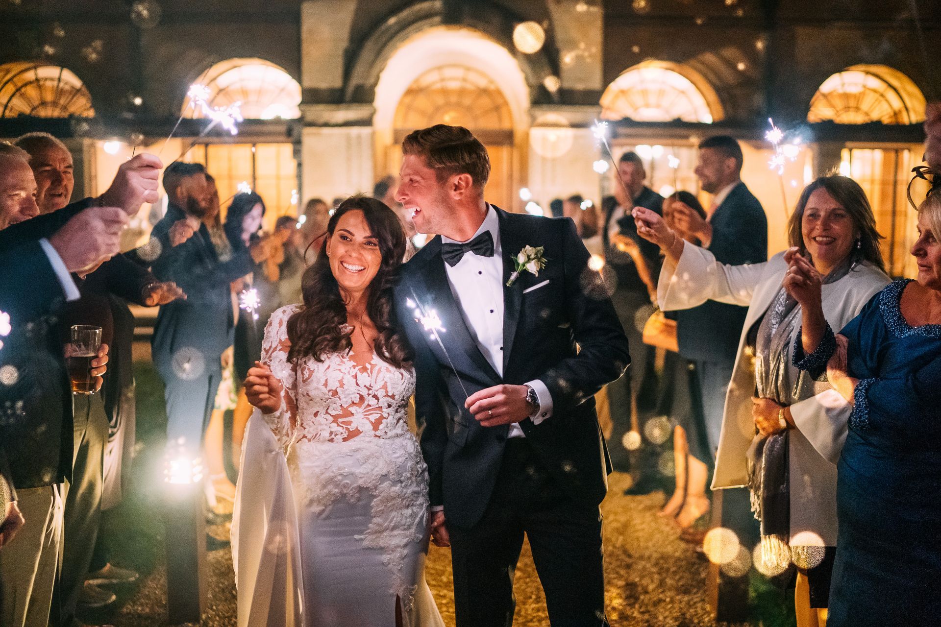 A bride and groom are walking through a crowd of people holding sparklers.