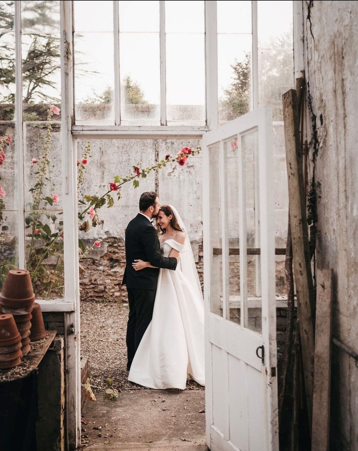 A bride and groom are standing next to each other in a greenhouse.