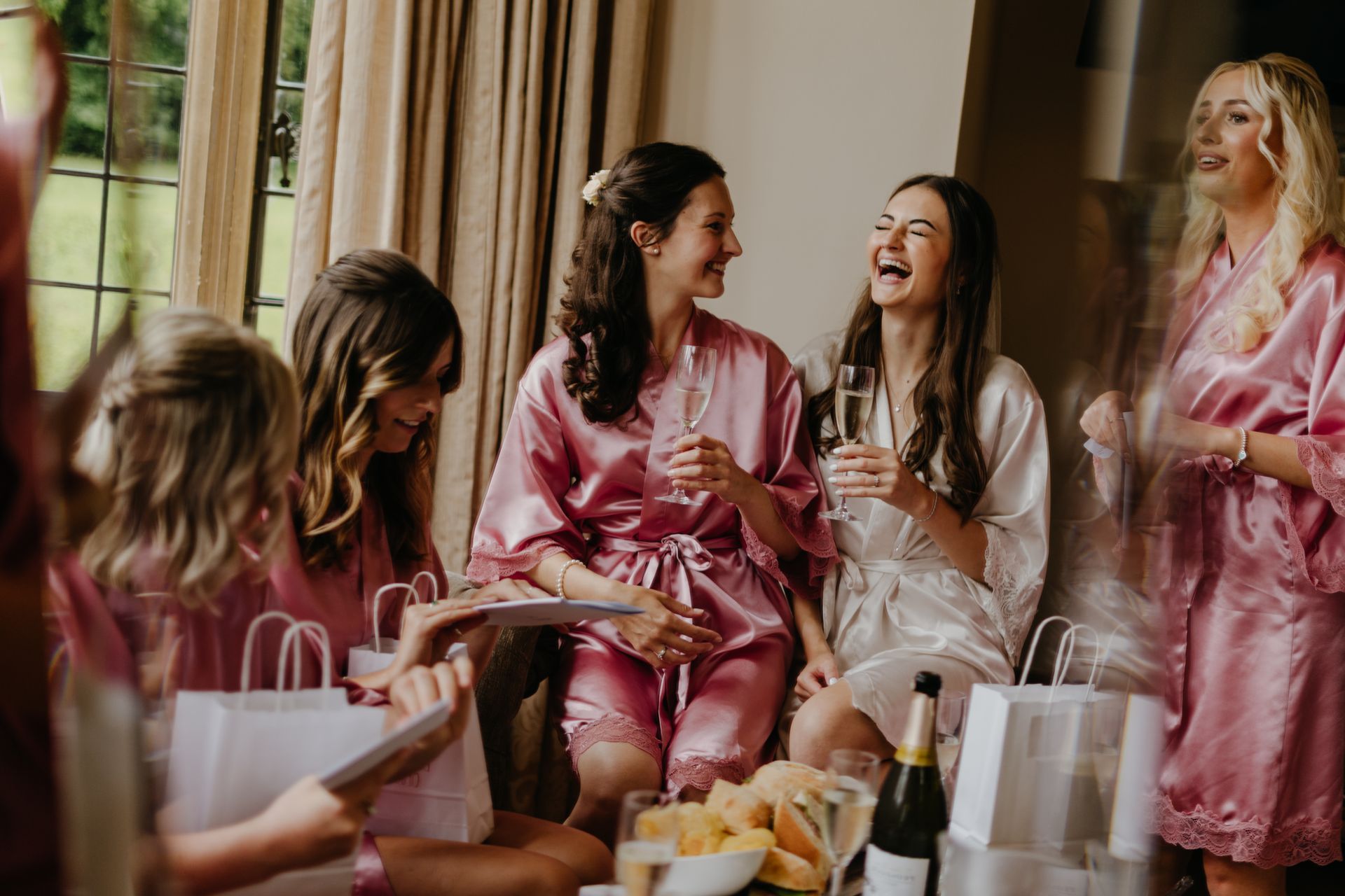 A group of women in pink robes are sitting around a table drinking champagne.