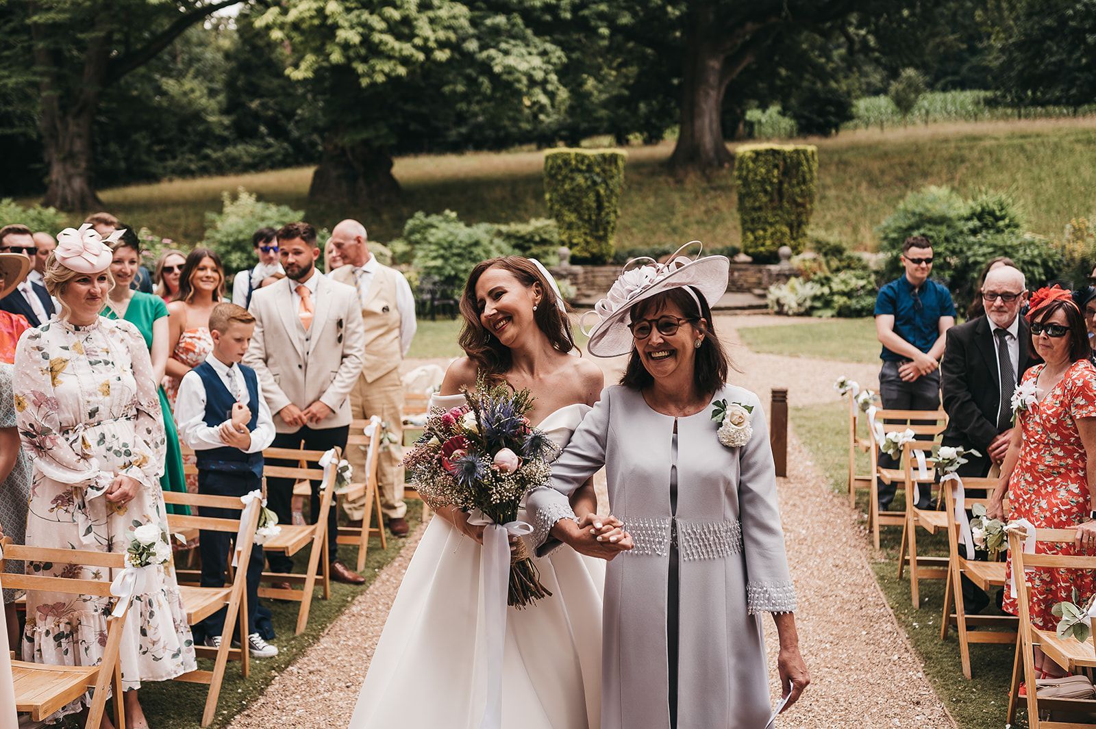 A bride and her mother are walking down the aisle at a wedding.