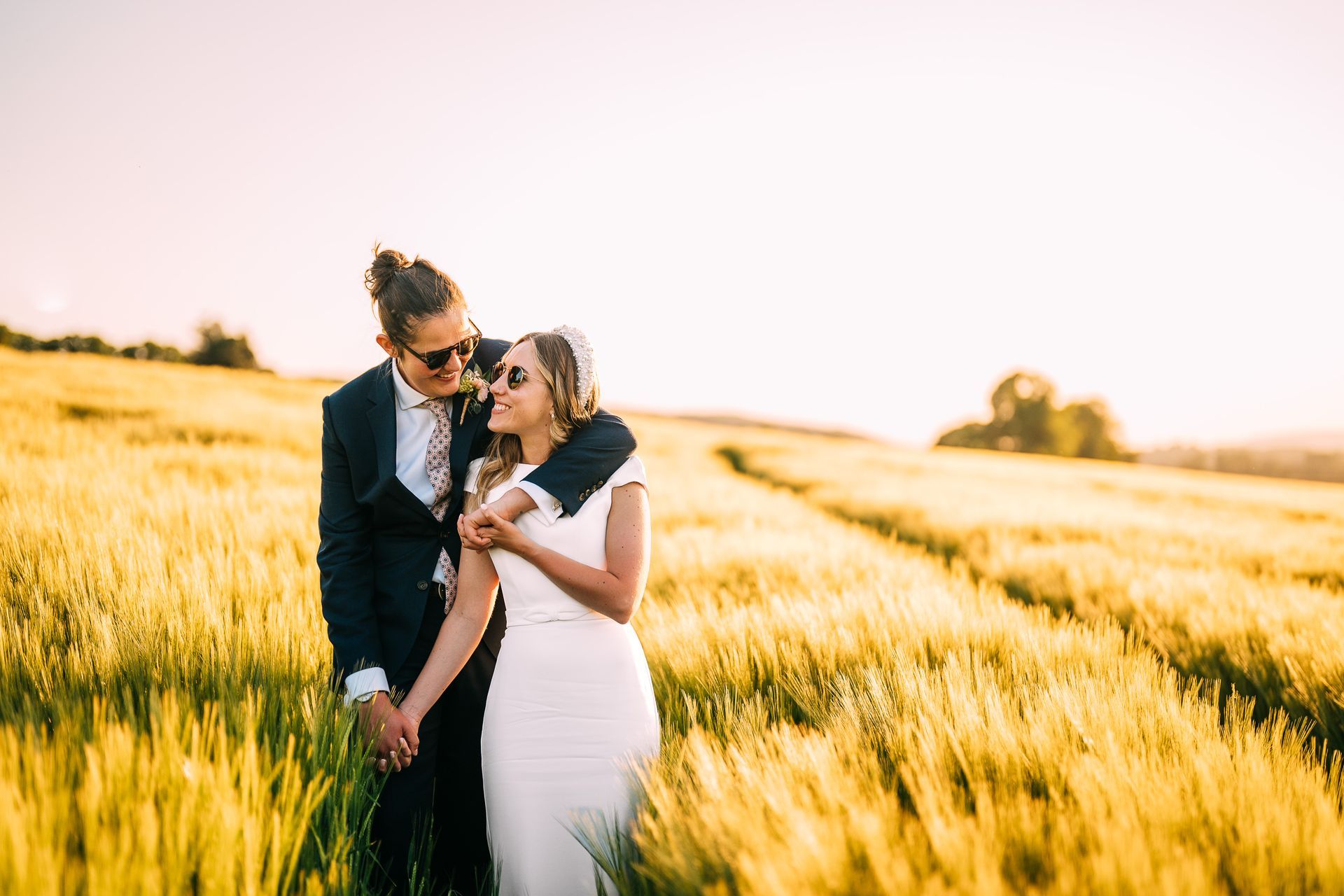 A bride and groom are standing in a field holding hands.