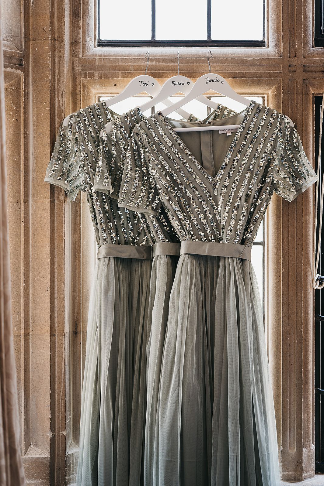 Two bridesmaid dresses are hanging in front of a window.