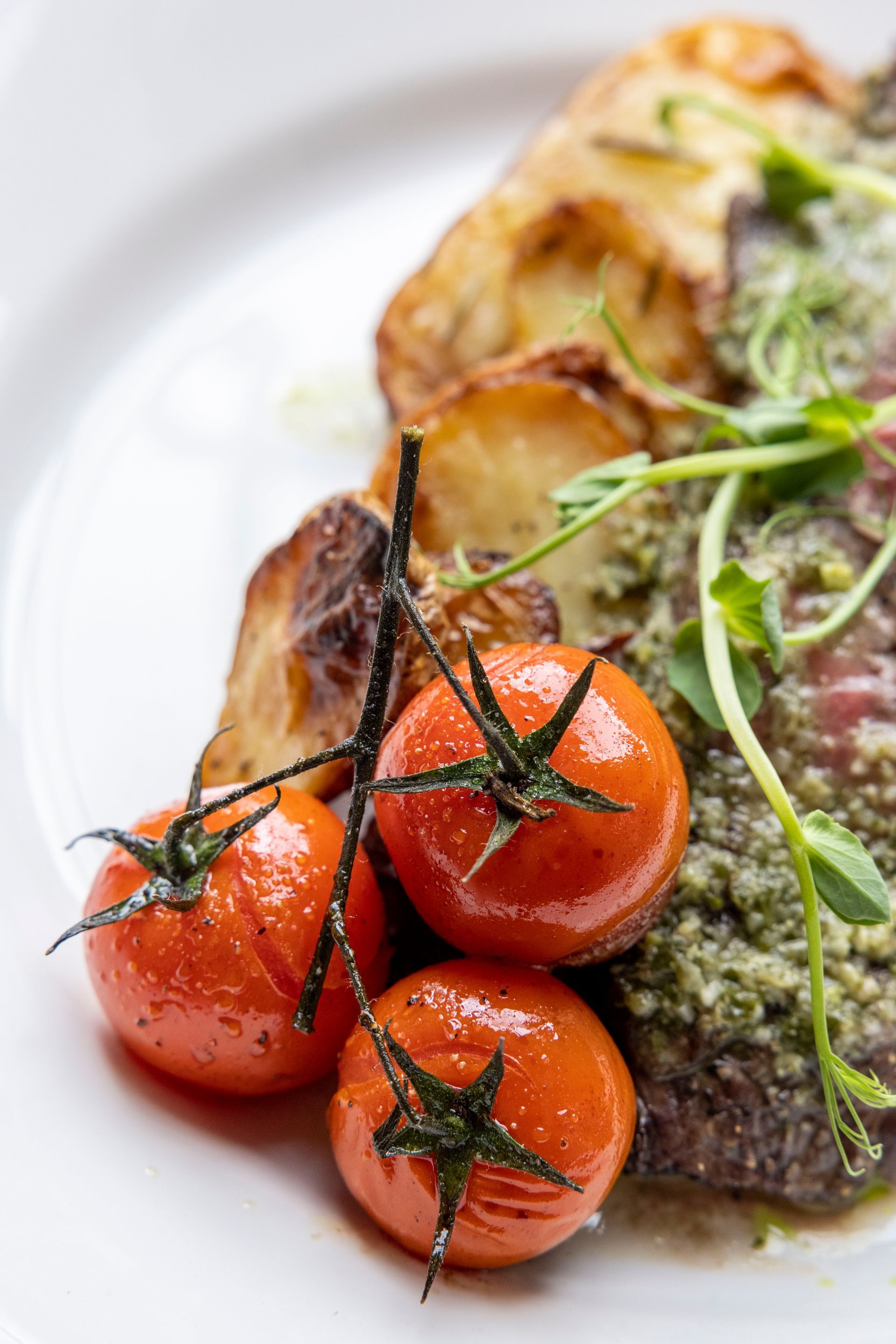 A close up of a plate of food with tomatoes and potatoes on a table.