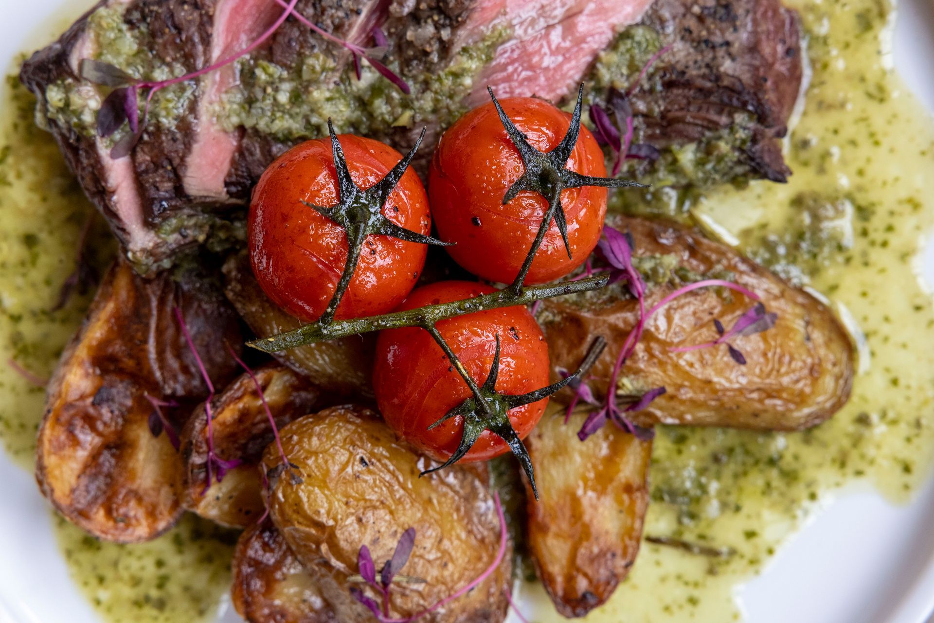 A close up of a plate of food with tomatoes and potatoes on a table.