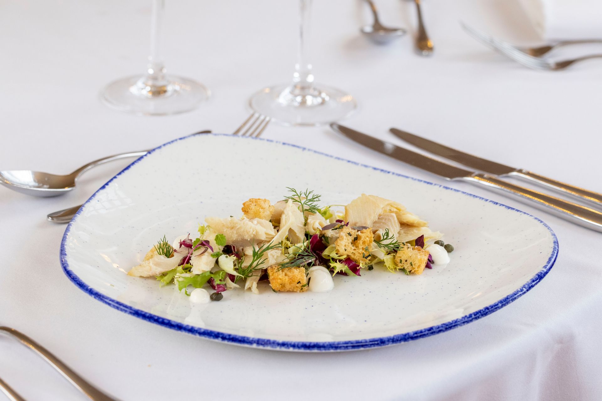 A white plate topped with a salad on a table with silverware.