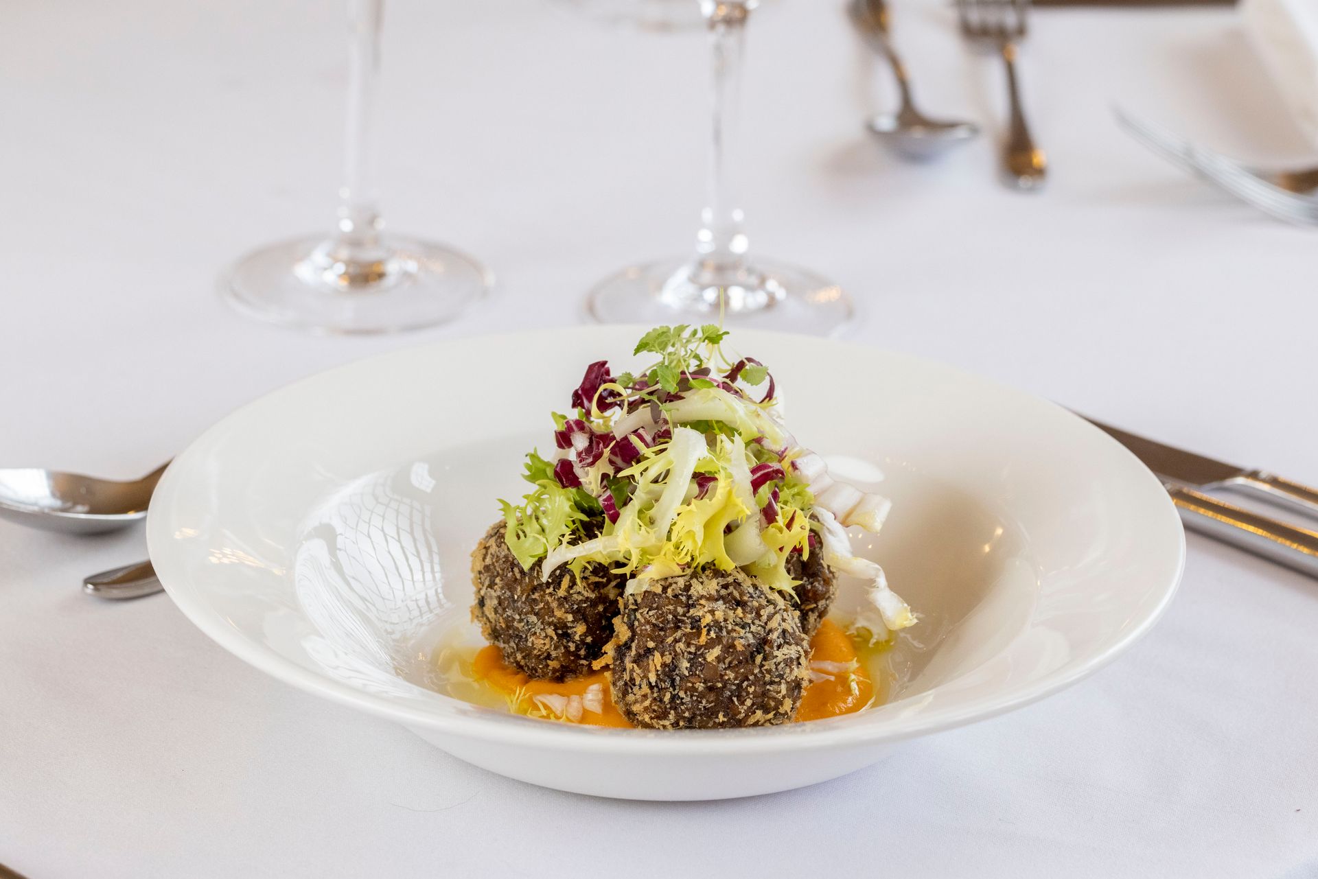 A white bowl filled with meatballs and vegetables on a table.