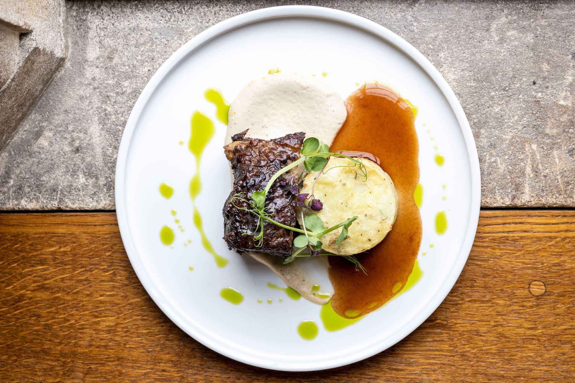 A white plate topped with a piece of meat and mashed potatoes on a wooden table.