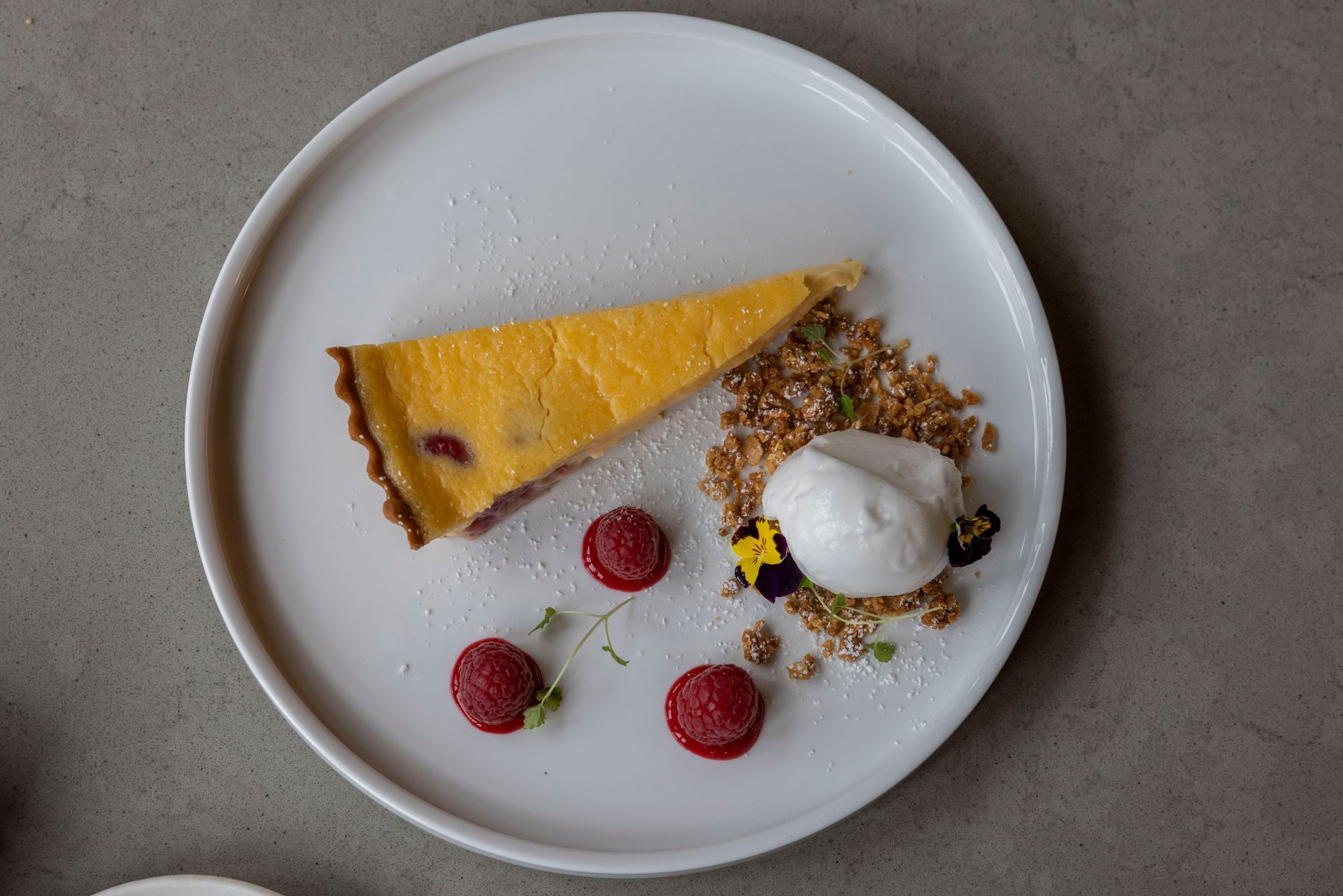 A white plate topped with a slice of pie and raspberries.