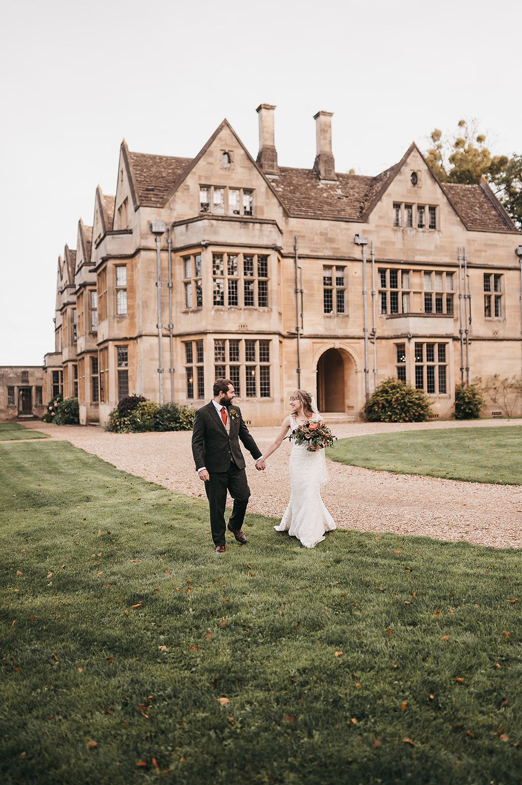 A bride and groom are walking in front of a large building holding hands.