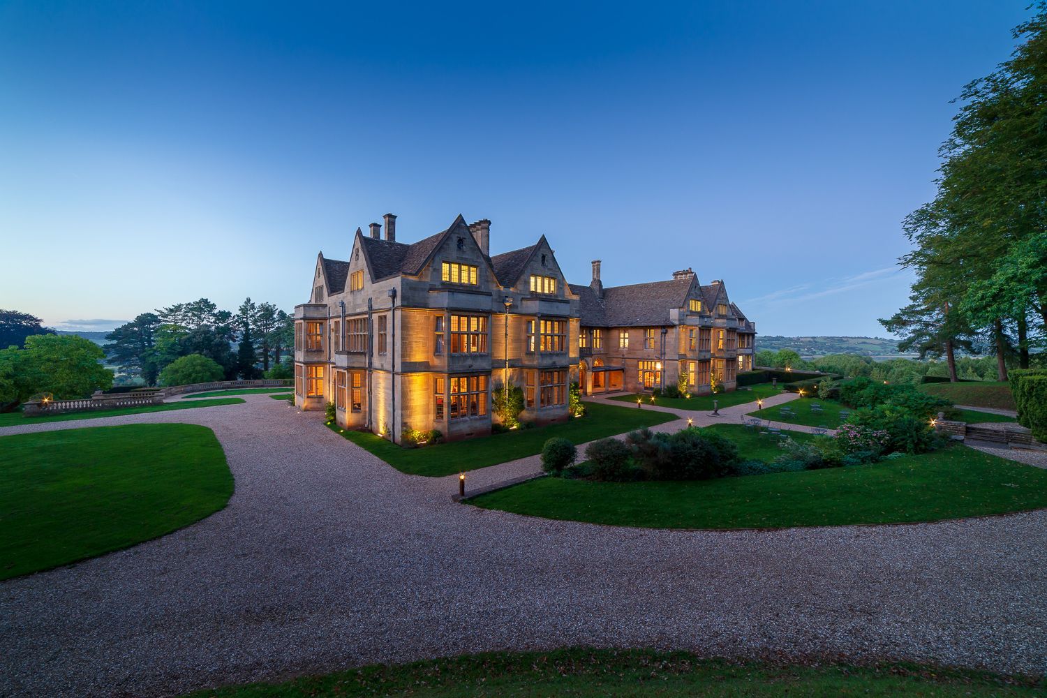 A large house is lit up at night with a gravel driveway leading to it.