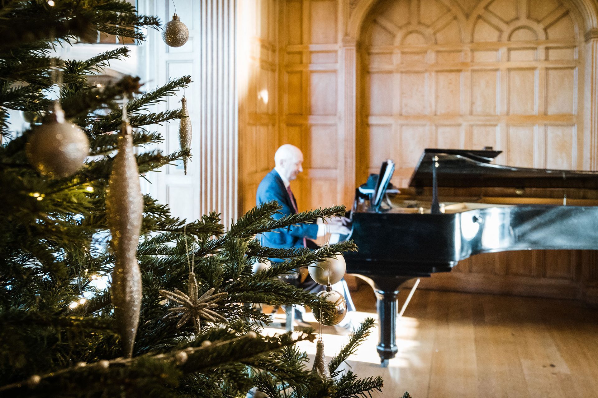 A man is playing a piano in front of a christmas tree.
