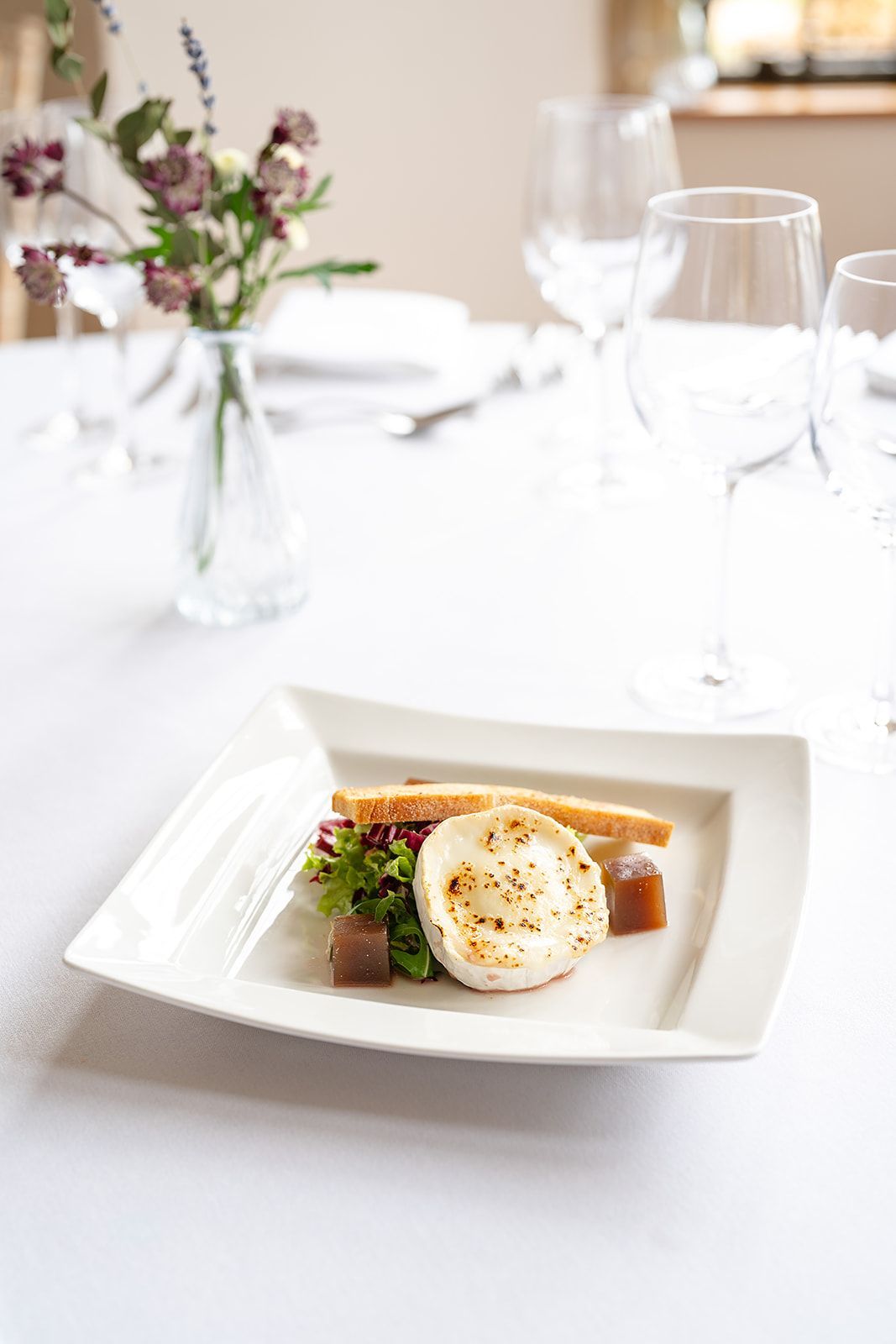 There is a plate of food on a table with a vase of flowers in the background.